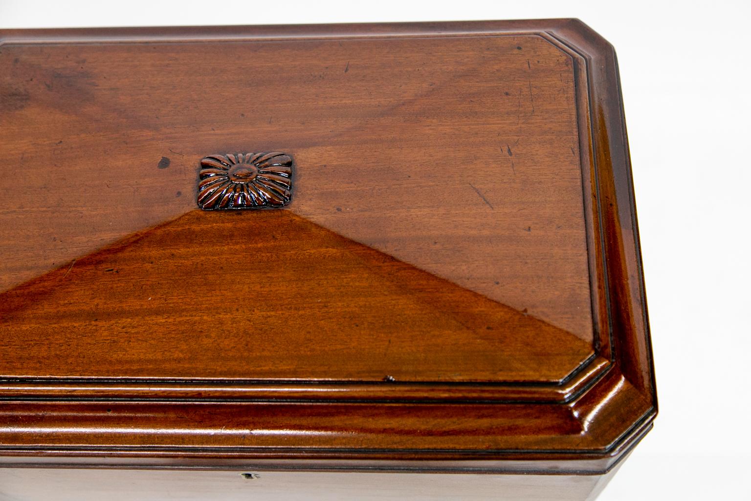 William IV mahogany tea caddy with a hand blown mixing bowl. There are two compartments with a section for serving spoons. It is trapezoid shaped on a carved stem platform base and small bun feet.