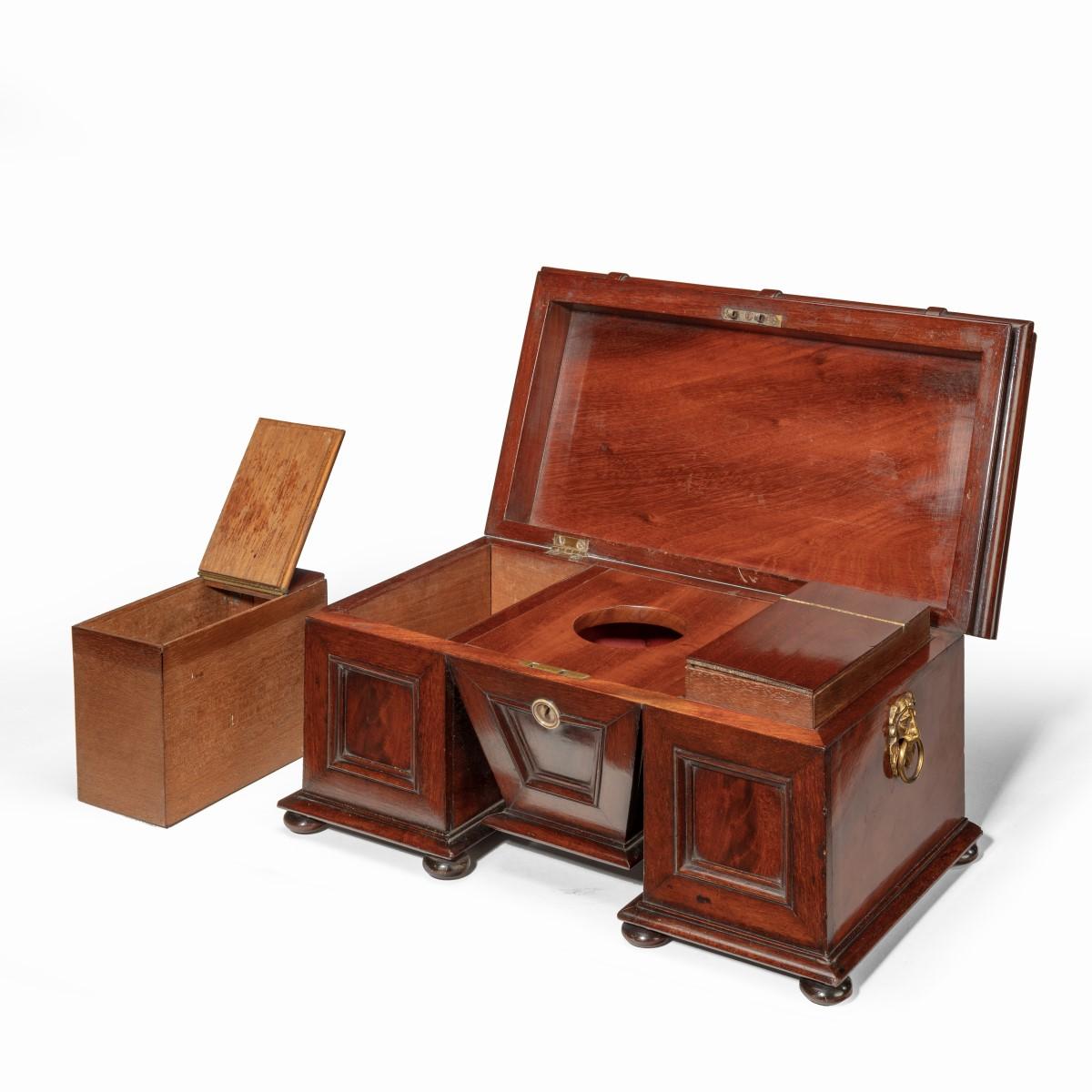 An unusual William IV mahogany tea caddy in the form of a pedestal sideboard with a hinged lid opening to reveal a central well for a mixing bowl (now missing) flanked by two removable tea containers, all raised on bun feet and with applied brass