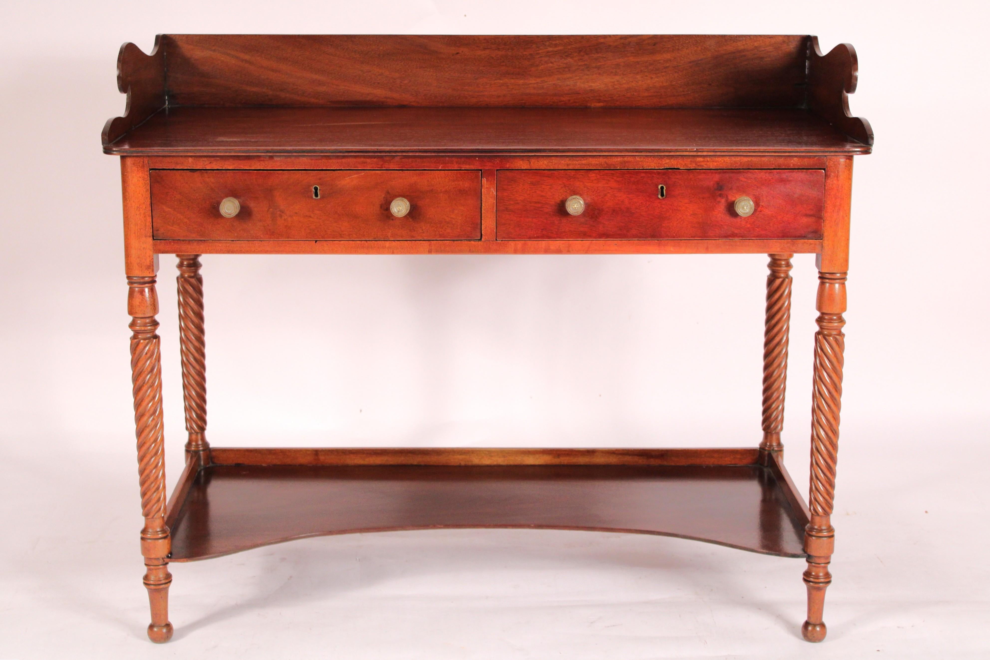 William IV mahogany washstand / drinks table, circa 1840. With a mahogany back splash, a rectangular serving area, two frieze drawers with brass knobs,
barley twist front and rear legs that are joined by a concave shaped shelf, resting on turned