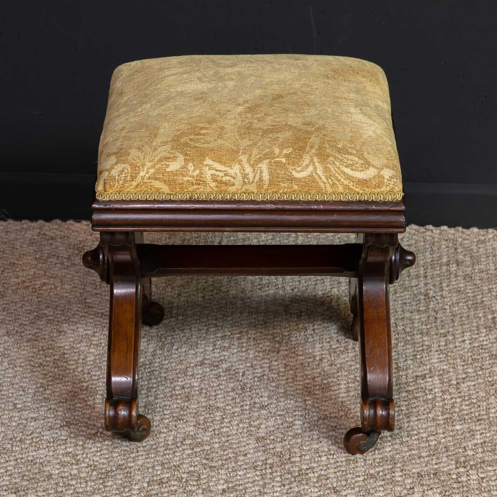 A William IV mahogany X-framed stool of small proportions. One or two interesting features like the scroll feet and central carved bosses make it a cut above average. Very solid and sturdy with the gold patterned draylon being in very good