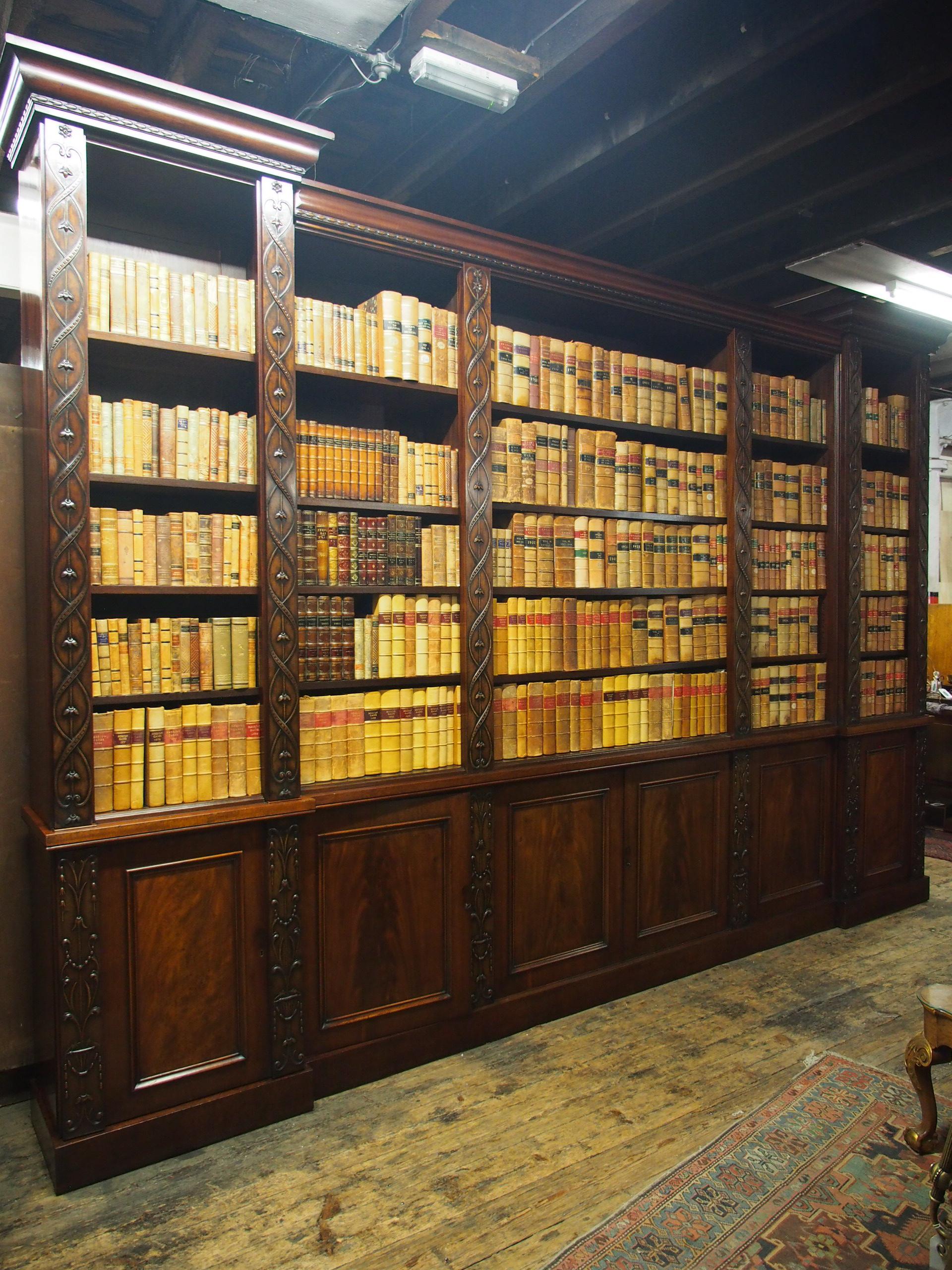 William IV reverse-breakfront, open mahogany bookcase, circa 1830. The stepped, cavetto cornice over a neat frieze with carved husk chains. The 4 narrower open bookcases flank the wide central bookcase, each with 4 adjustable mahogany shelves and