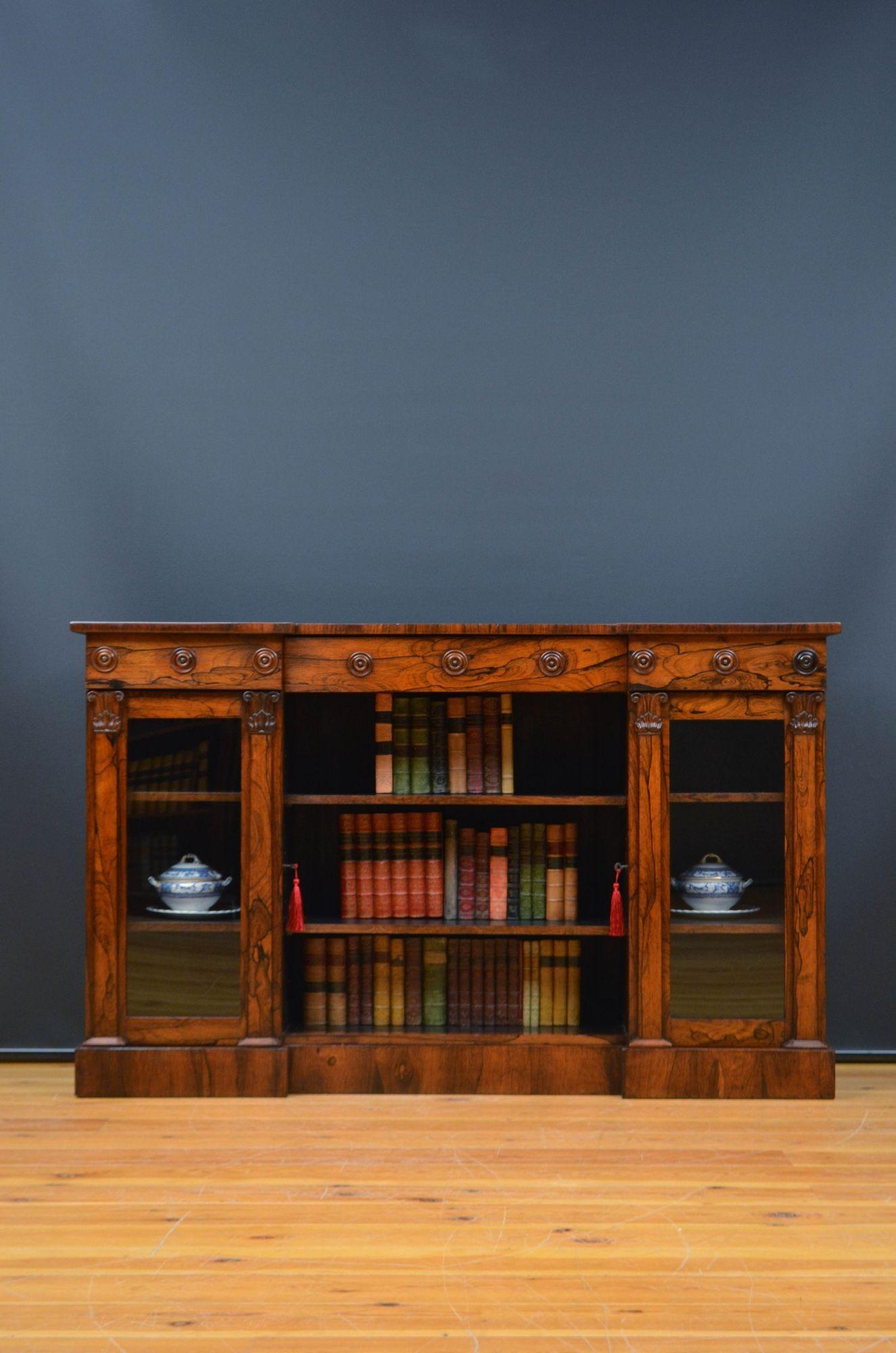 Sn5601 Antique English William IV rosewood bookcase of inverted break front design, having well figured oversailing top above decorative frieze with a centre drawer and open section below, flanked by two glazed door each fitted with original working