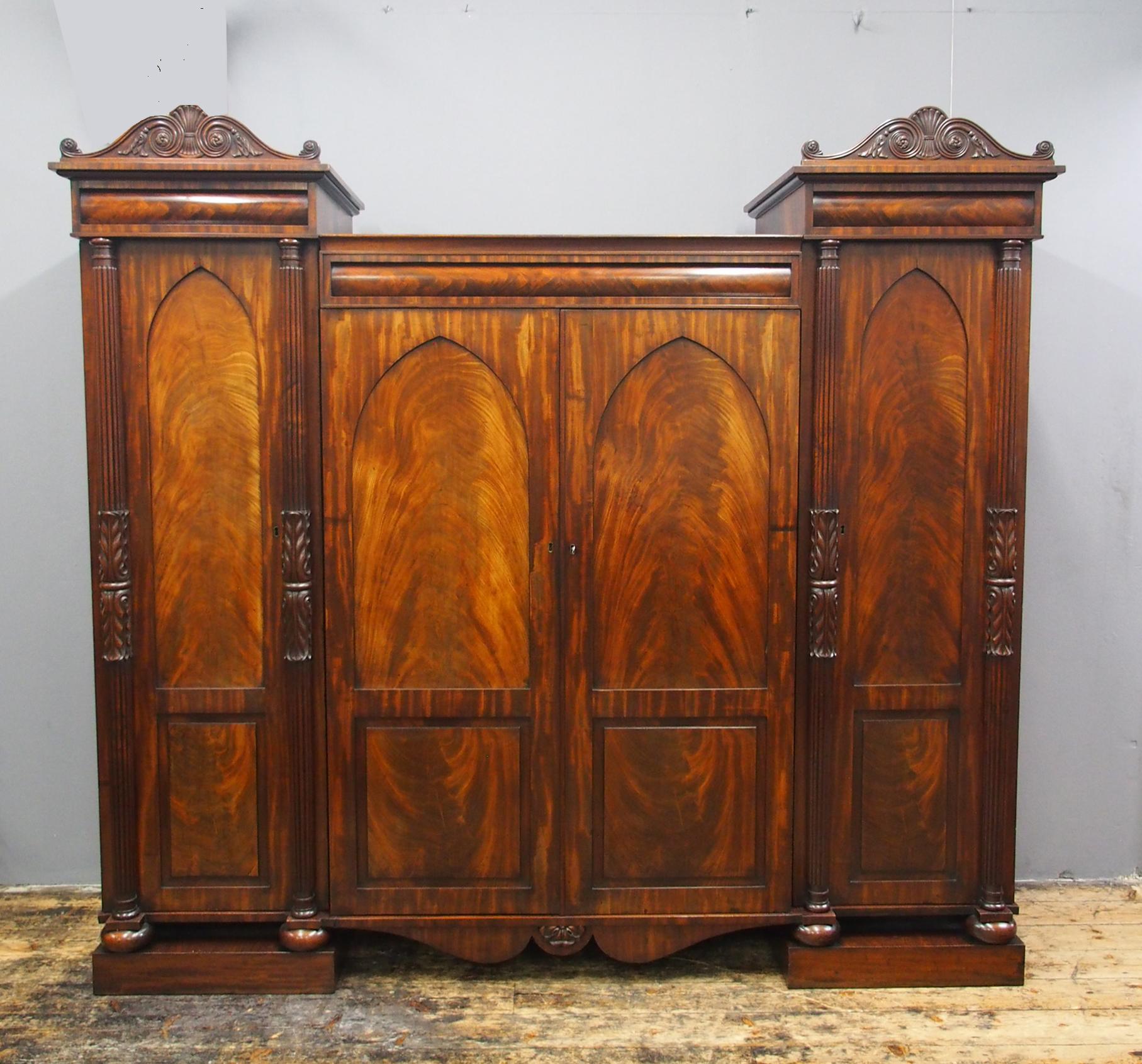 William IV Scottish mahogany 4-door wardrobe, circa 1830. With a cushion molded cornice and foliate carved pediments leading on to raised sides, it has Gothic arched panel doors in flame mahogany. These are flanked by fluted and acanthus carved