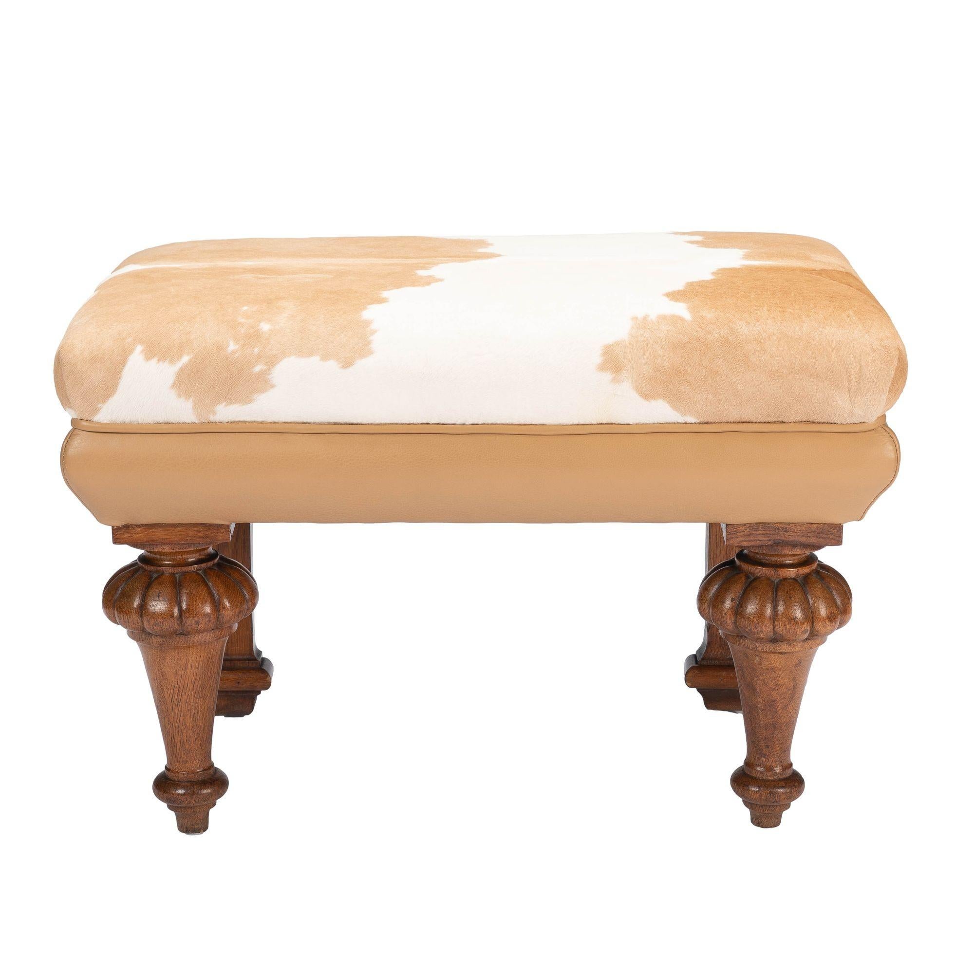 English William IV leather & hair on hide calf skin upholstered window bench on English oak legs. The bench features conical turned and melon carved front legs with Neoclassic pilaster rear legs supporting an upholstered seat frame covered in