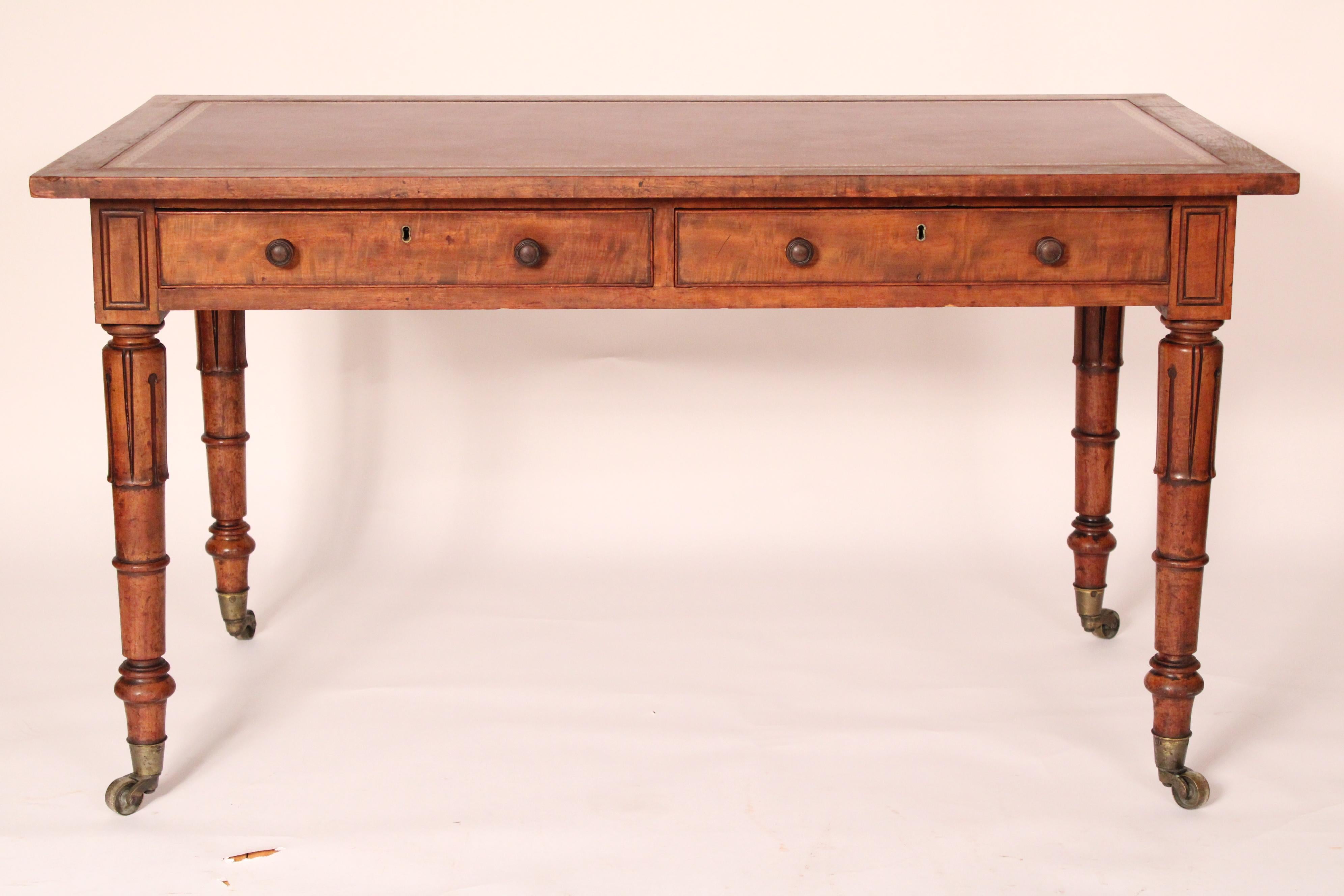 Antique William IV walnut writing table, 19th century. With an inset tooled leather top and walnut borders, two frieze drawers on front side and two false drawers on back side, supported on 4 turned, carved and tapered legs, ending in brass casters.