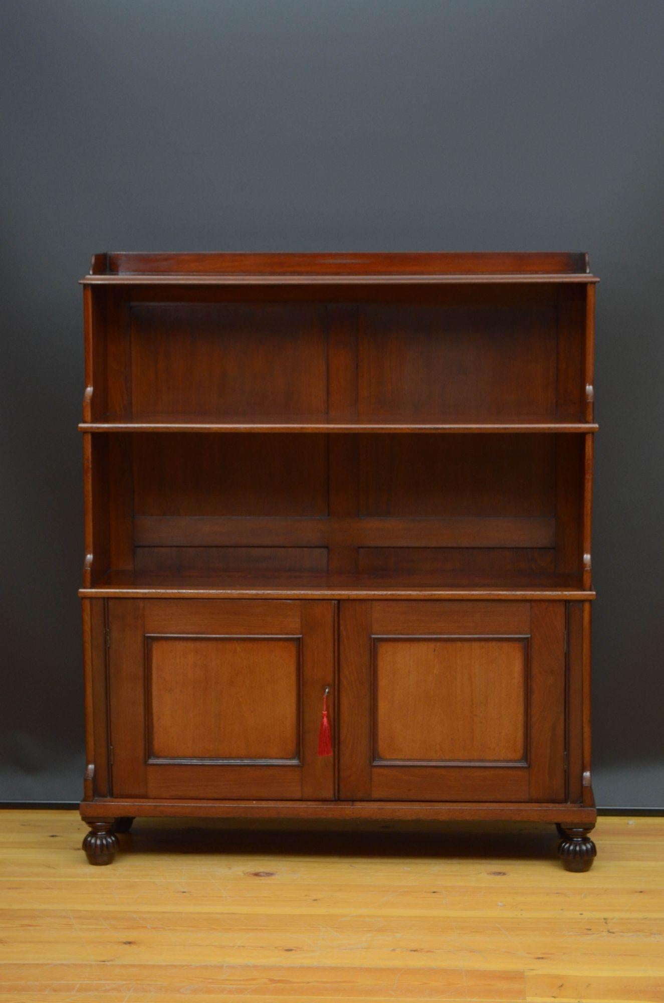 St014 Fine quality William IV mahogany bookcase, having shaped upstand, waterfall shelf arrangement and a pair of panelled cupboard doors fitted with original working lock and a key and enclosing shelf, all standing on fluted bun feet. This antique