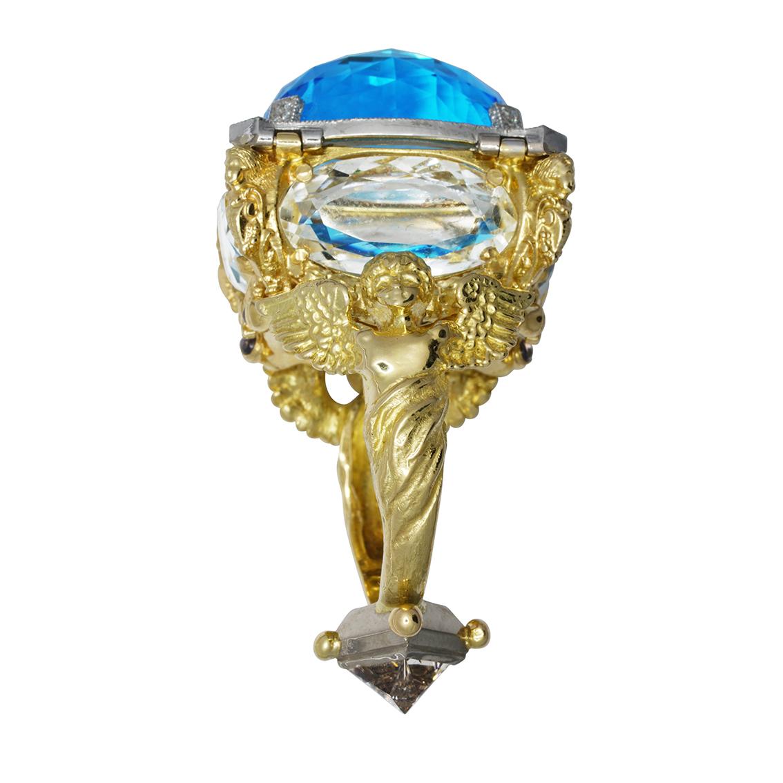 The Poseidon Ring is a huge 18ct yellow gold piece featuring a closing chamber build from a central vivid blue 23 carat topaz, and 4 white topaz which make up the other four windows. 

There is an additional hidden 1.5 carat princess cut diamond on