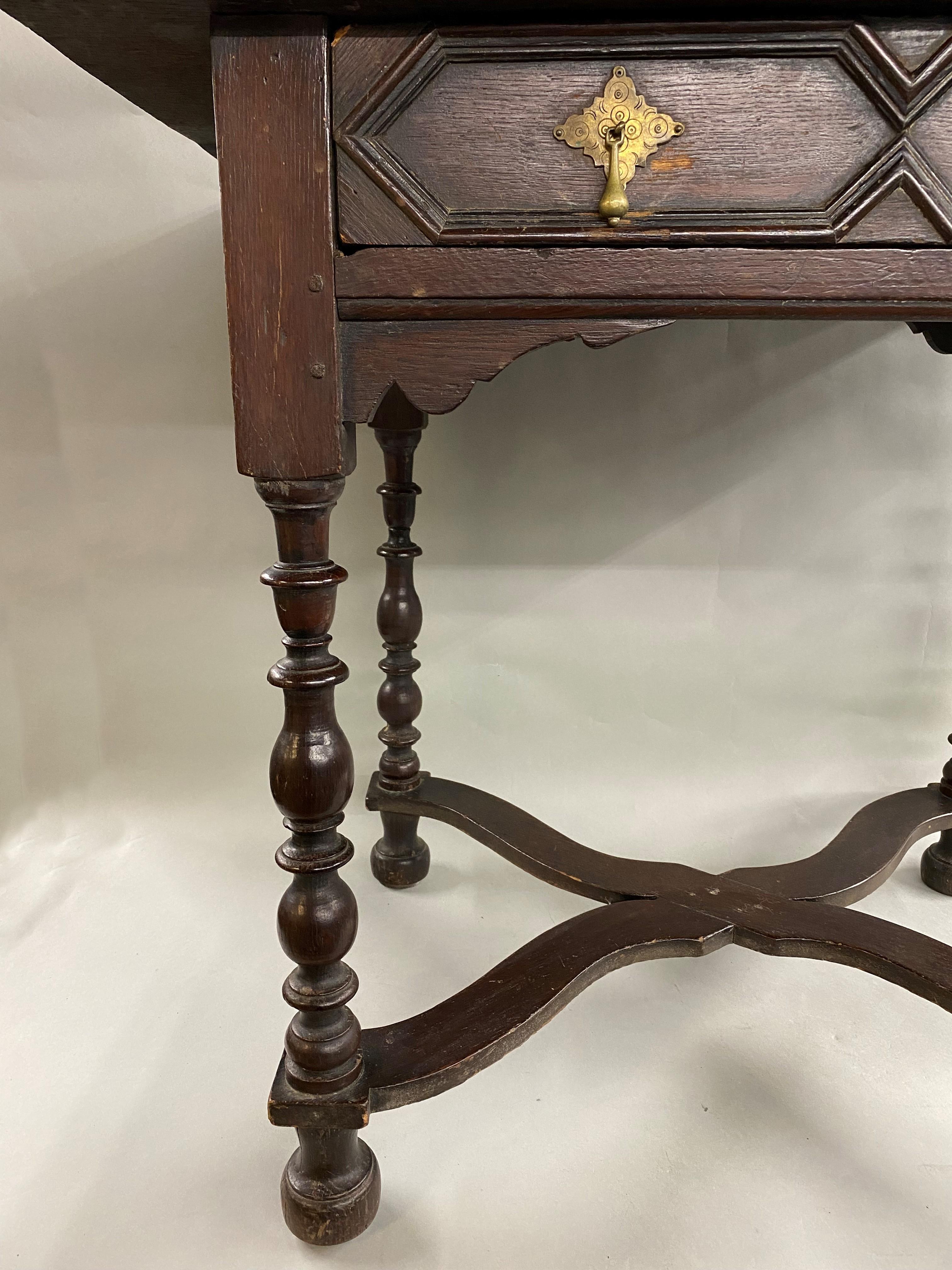 A William & Mary one-drawer oak dressing table with rectangular molded edge top surmounting a single frieze drawer with raised hexagonal panels and brass drop pulls, supported by four nicely turned legs with a shaped base stretcher. The table dates