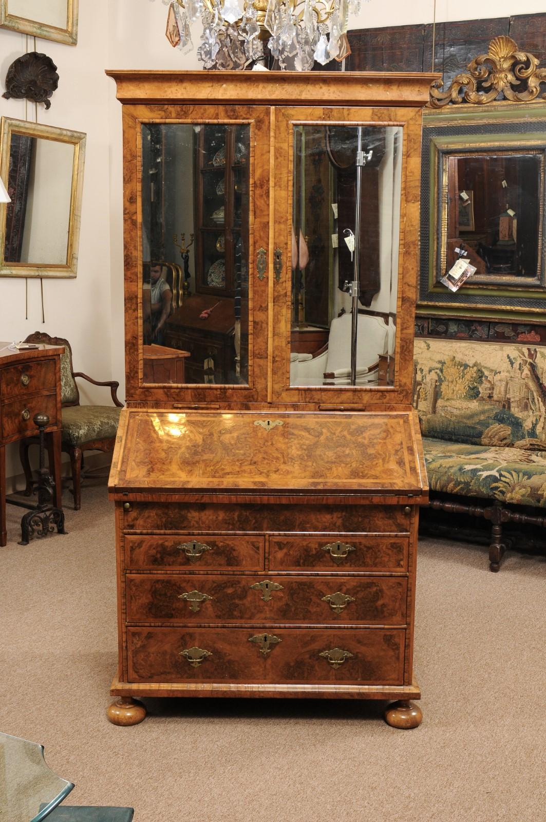 The William & Mary style burled walnut English bureau bookcase with beveled old mirror doors and bureau slant front enclosing fitted interior and green embossed leather writing surface. Below with two short drawers and two long drawers with brass