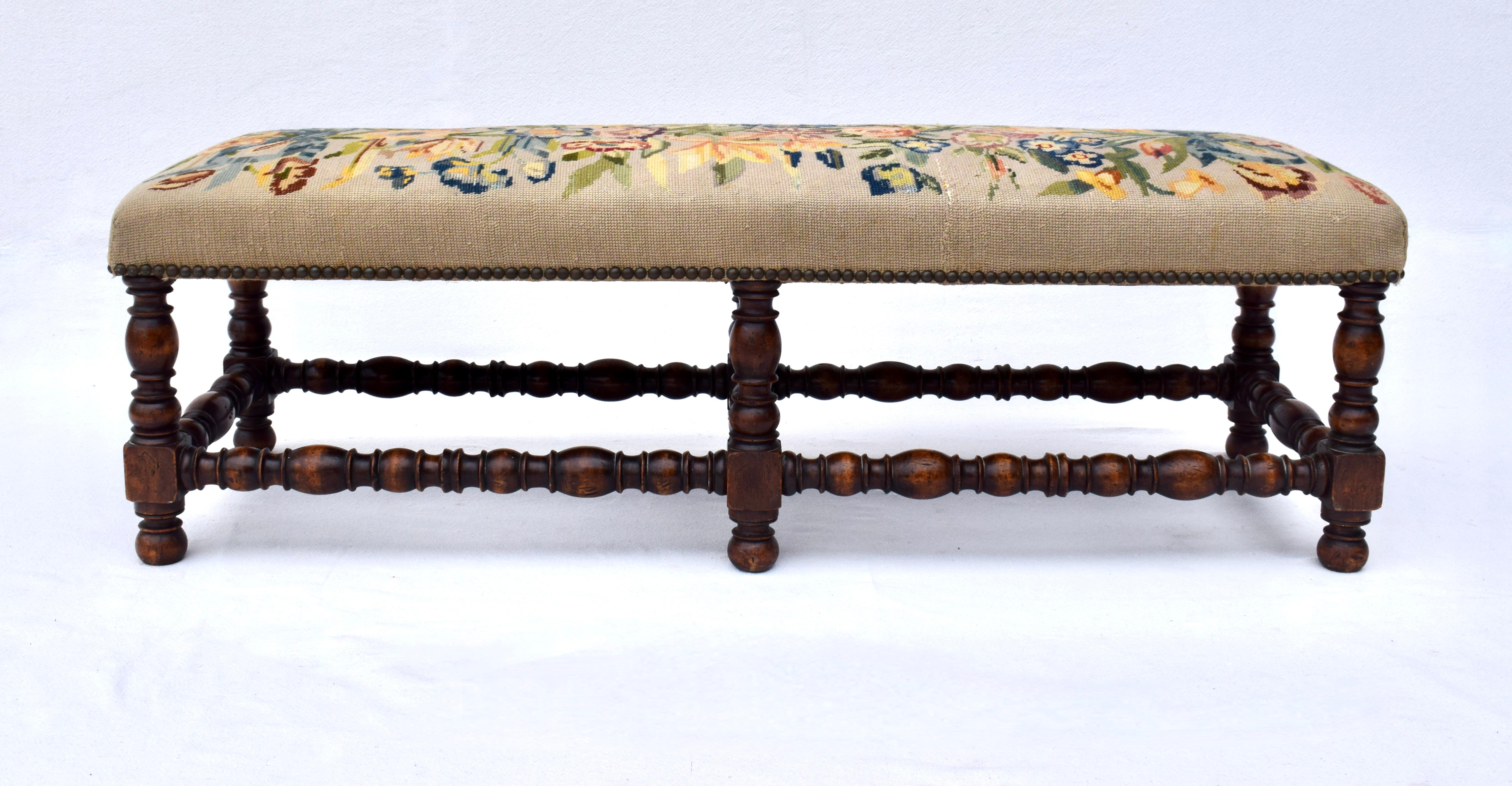 An early 20th Century William and Mary style walnut hearth bench with turned legs and stretchers. The Needlepoint top shows signs of wear boasting marvelous old world character. Height: 14.5
