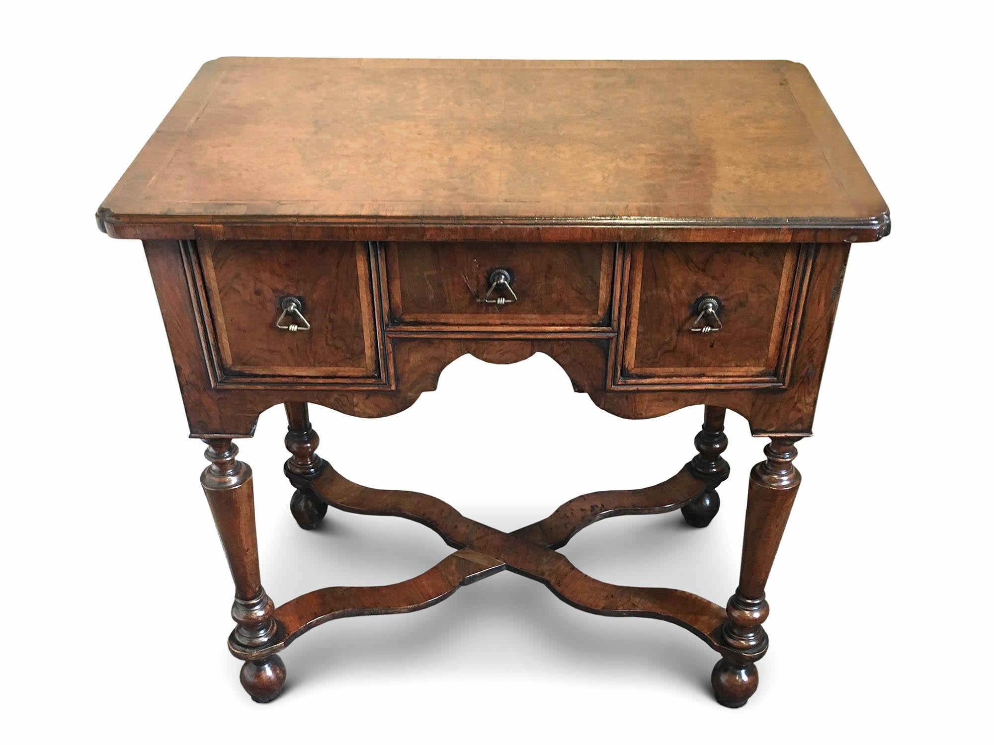 A William & Mary Walnut Lowboy, circa 1700 & later.
The top with cross banding and rounded corners, with three drawers, carved apron resting on four turned tapering legs joined by an X stretcher.

This item has been fully restored.