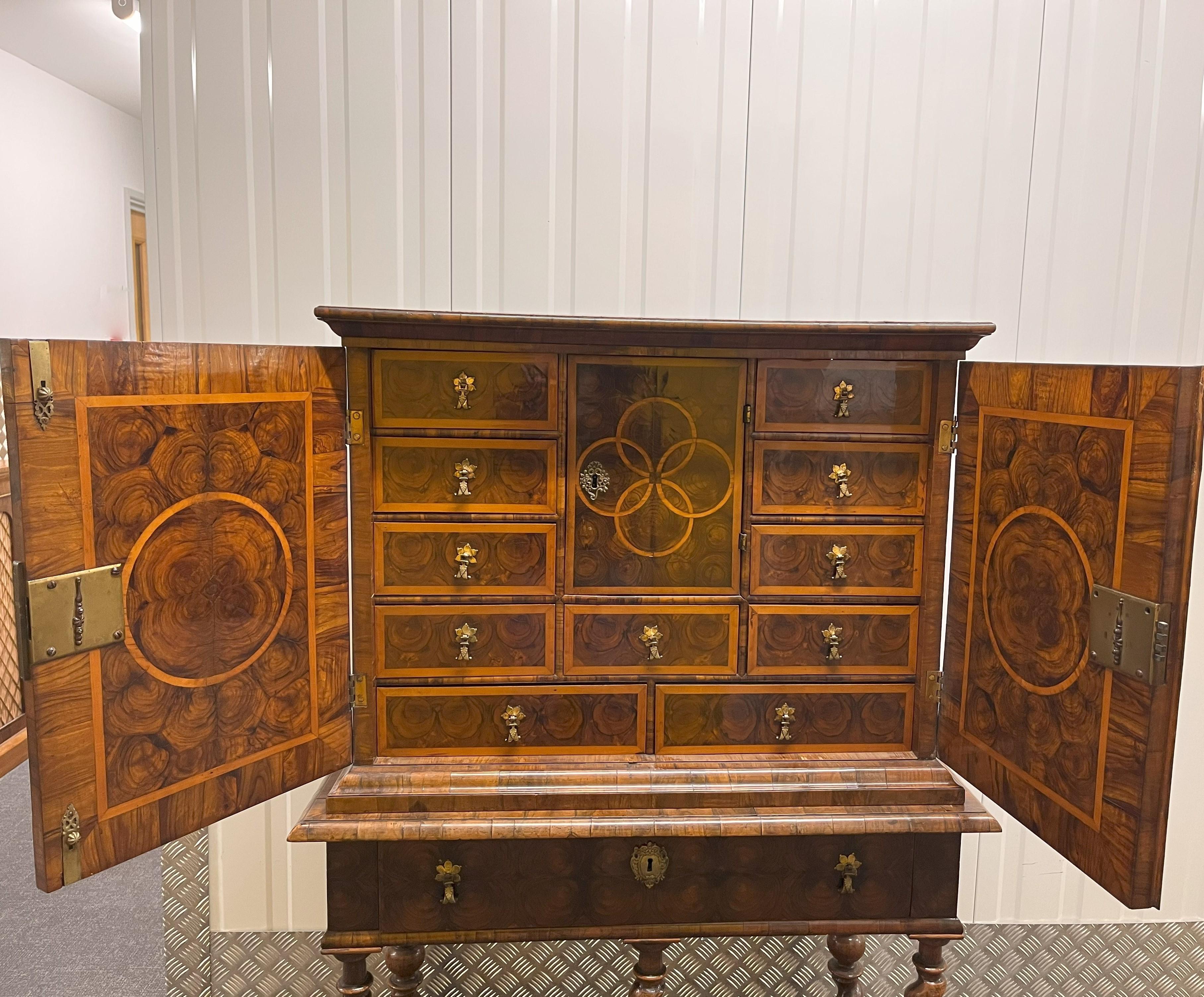William & Mary Walnut Cabinet on Stand, the cabinet veneered inside and out with oyster patterns within holly boarders and interlaced lines, the two doors enclosing eleven draws surrounding a central cupboard which encloses four draws, all fitted