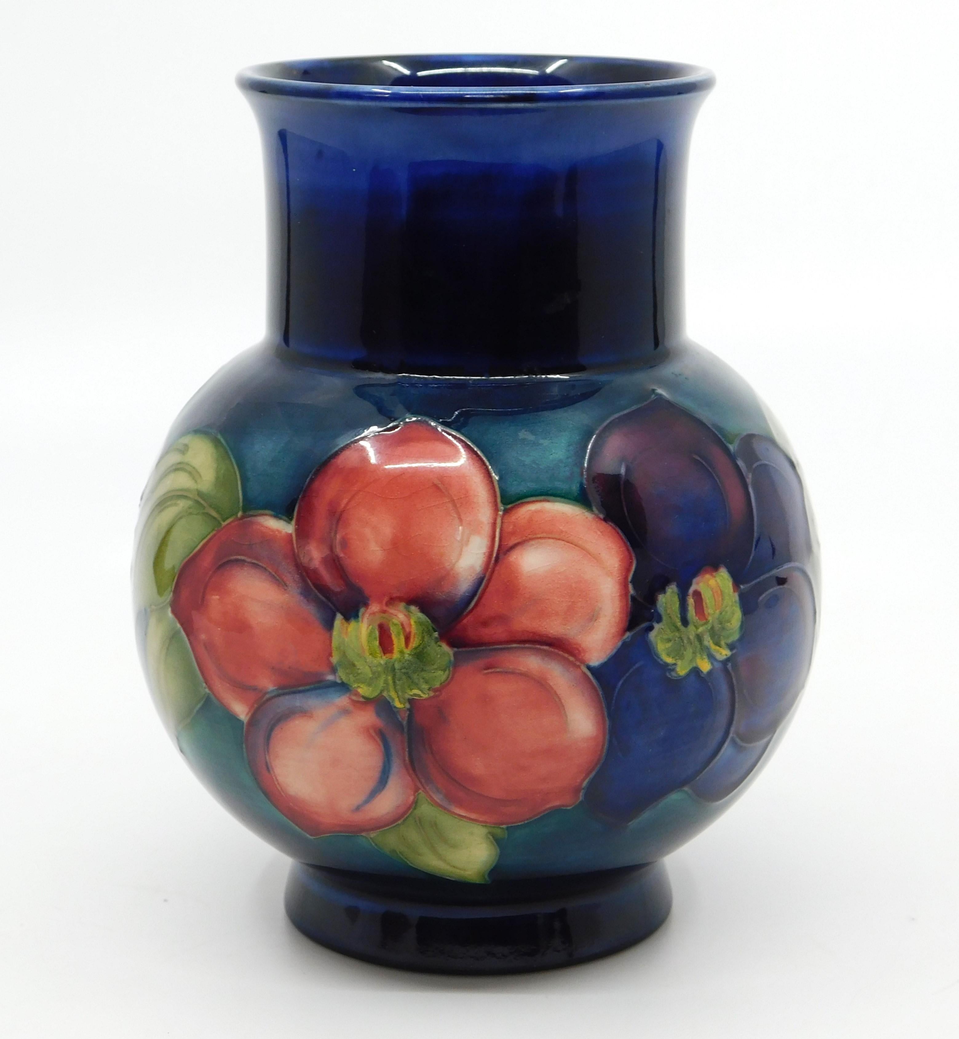 This beautiful art pottery vase was done by the Moorcroft Pottery company of England in circa 1940 using their signature deep cobalt blue ground and done in the 'Clematis' pattern.
Designed and produced by William Moorcroft It features fine tube