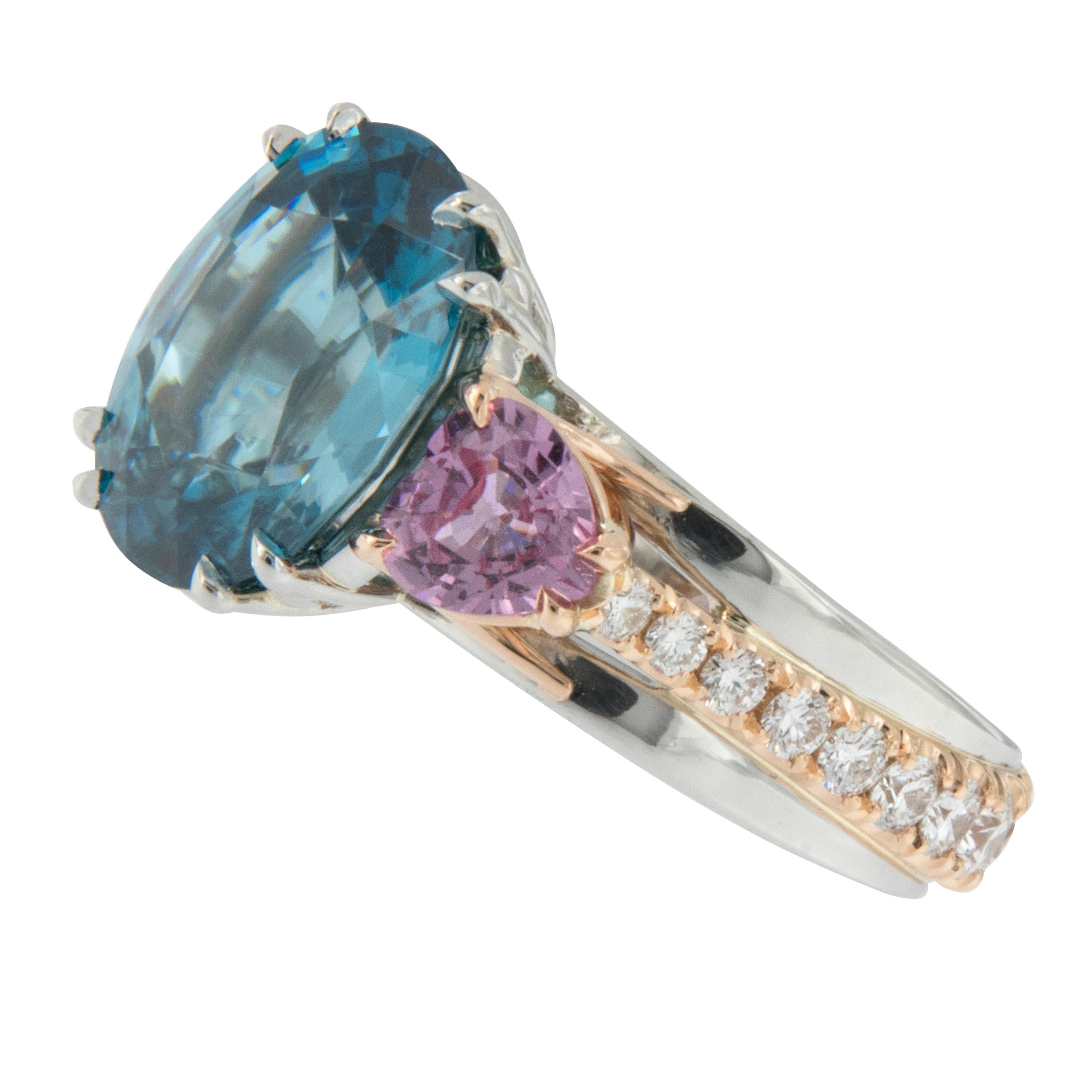 Perfectly paired in color is this hand fabricated ring by William Rosenberg! The intense blue of the Zircon plays against the intense pink sapphires which are further enhanced by the platinum & rose gold metals & diamonds. 7.85 Ct oval blue zircon,