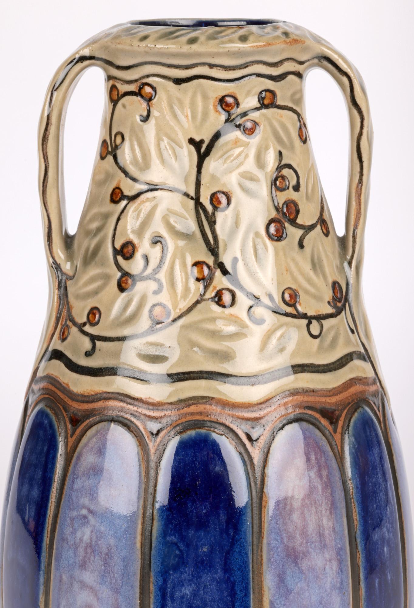 Eine stilvolle Doulton Lambeth Art Deco Vase mit zwei Henkeln von dem bekannten Künstler William Rowe aus der Zeit um 1918. Die Vase aus Steinzeug hat eine hohe, bauchige Form und steht auf einem schmalen, runden, unglasierten Fuß. Der untere Teil