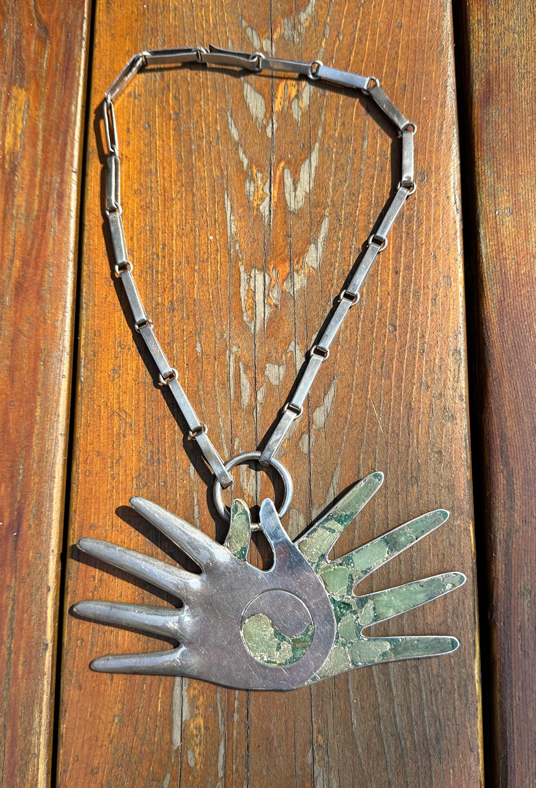 Date un capricho con una impresionante antigüedad William Spratling (estadounidense, 1900-1967)
Collar de mano con incrustaciones de plata de Taxco y chip de turquesa, 1965-1967. Diseñada como dos manos opuestas de plata e incrustaciones de piedra