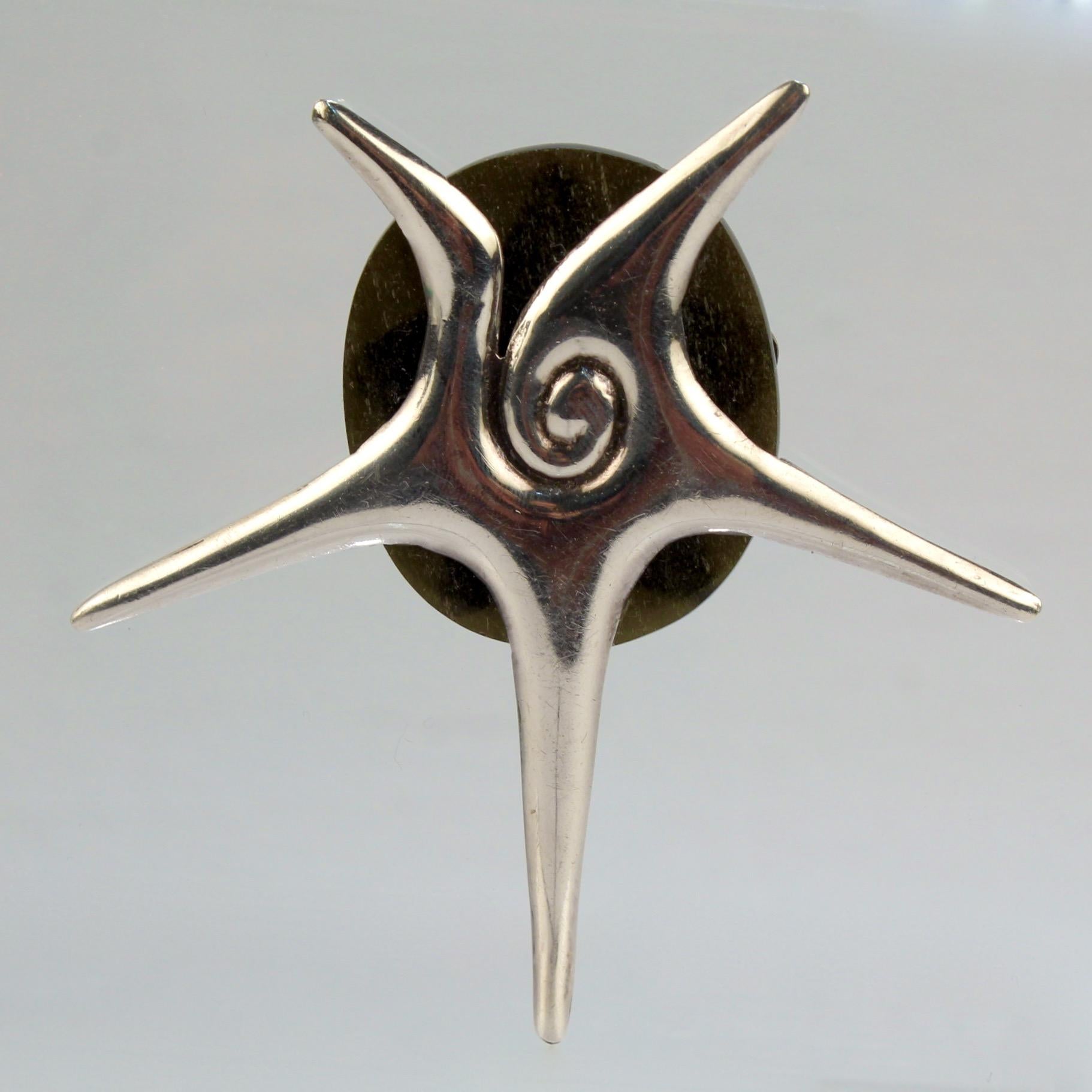 A fine William Spratling brooch or pin.

In the shape of a stylized conch shell supported by a dark green disc.

Comprised of sterling silver and a smooth polished dark green gemstone (that we believe to be aventurine quartzite.)

Simply compelling