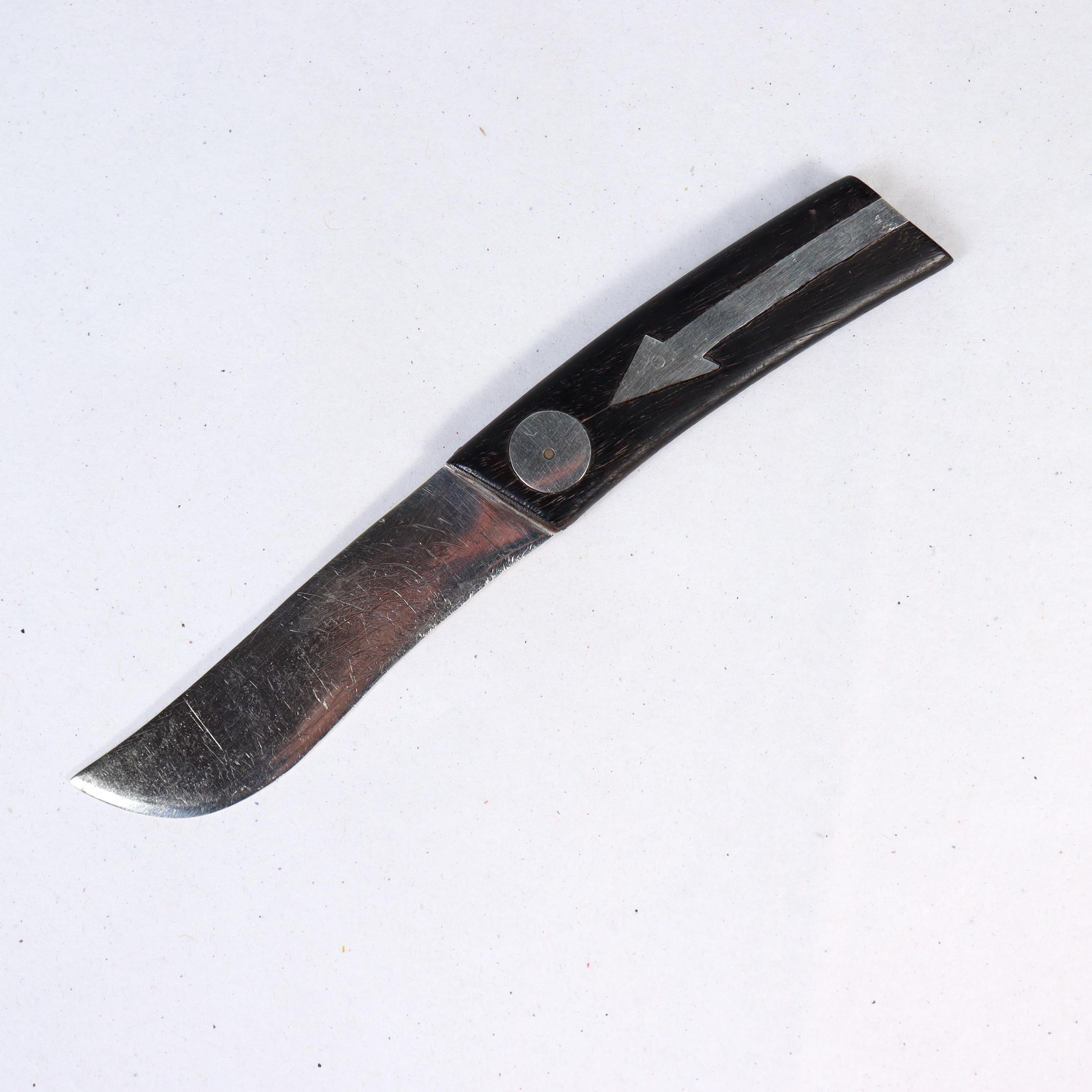 A fine Mexican Modernist cheese or bar knife.

By William Spratling.

In sterling silver. 

With a shaped sterling silver blade and an ebony handle with sterling silver inlaid elements, including arrows and discs.

Simply a great, diminutive knife