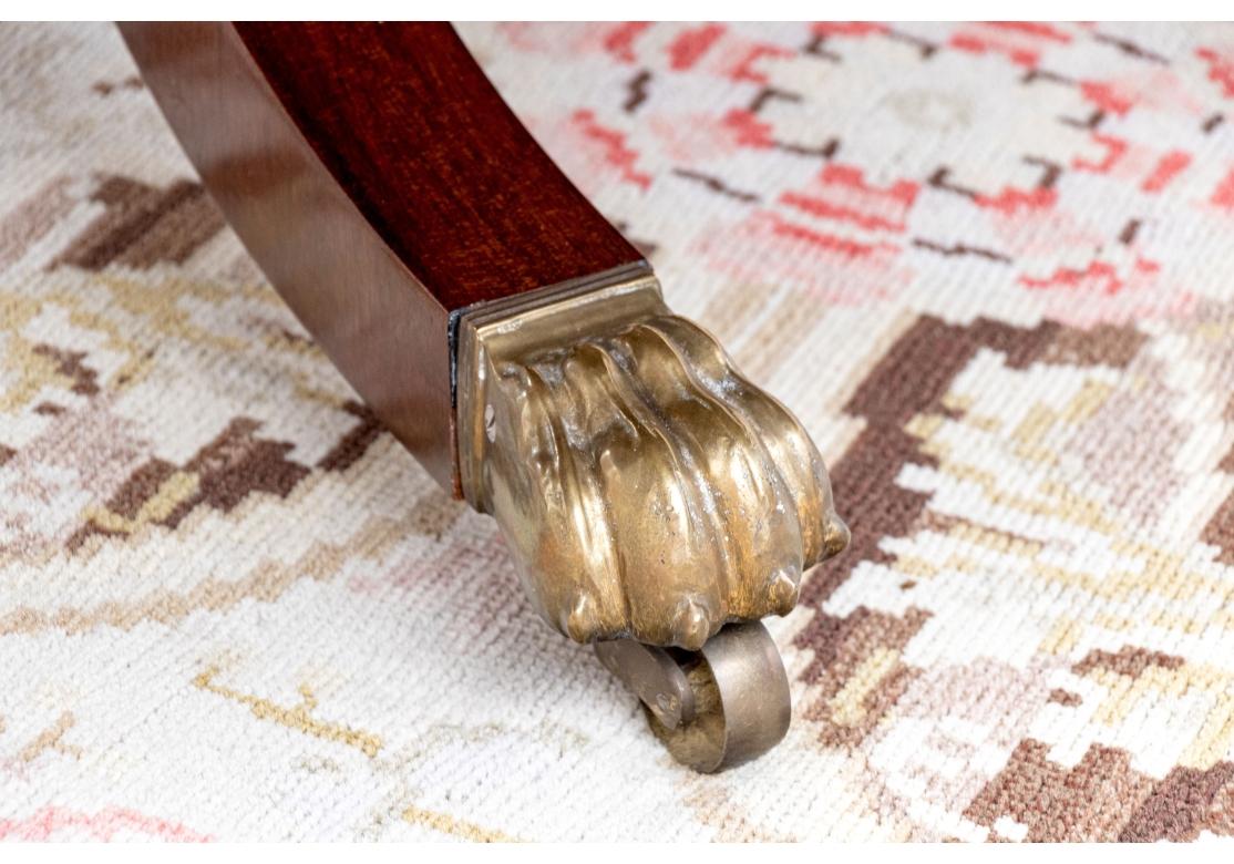 The table stands on four curved legs with brass lion paw form feet and brass casters. The curved legs have a lower tiered shelf with the circular table top above. The circular table with five extension leaves which are all curved and fit around the