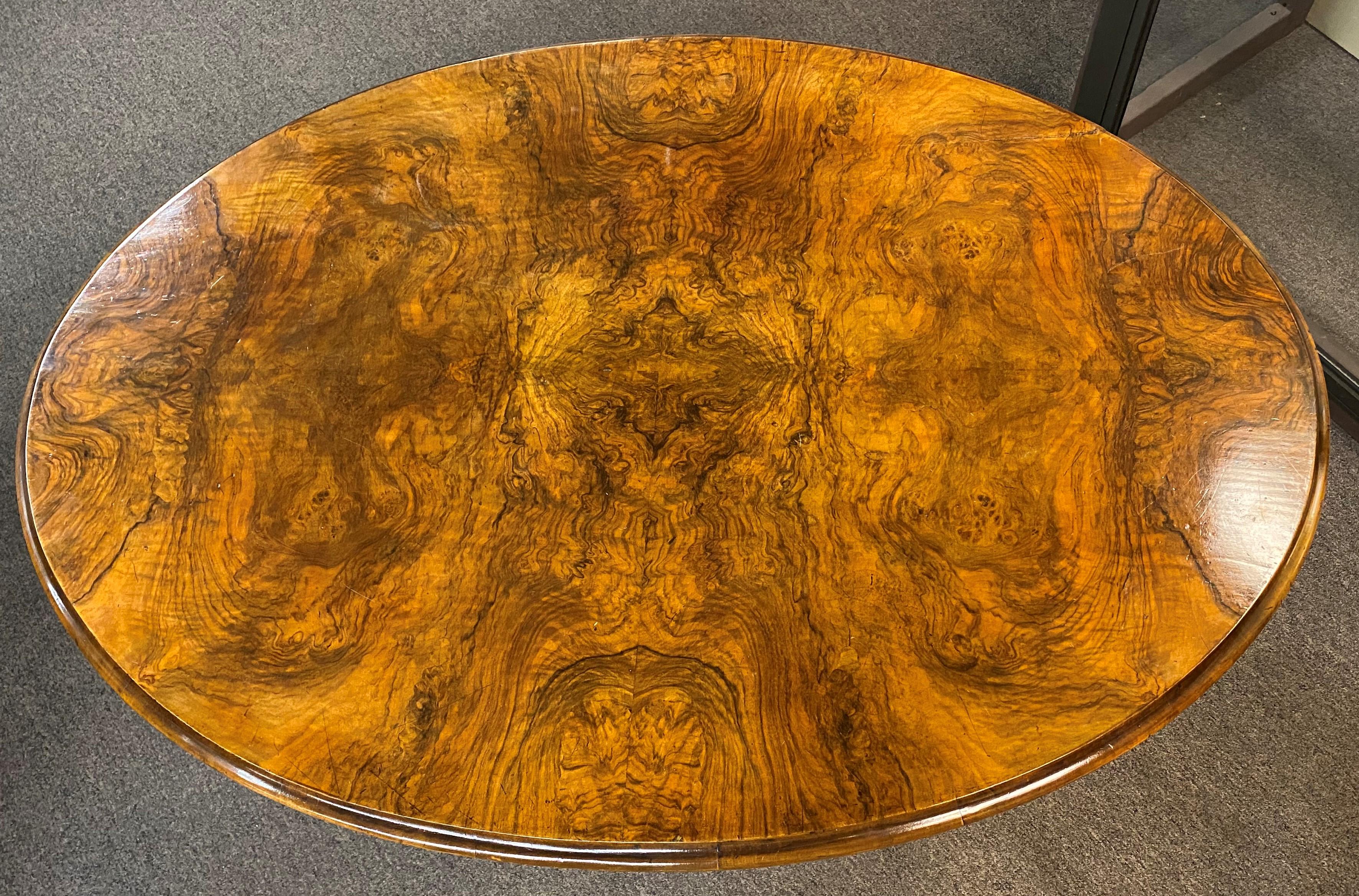 A fine example of a burled walnut veneer oval tilt top breakfast table or center table with a nicely carved four leg pedestal terminating with brass casters. An oval William Wallace & Company, London tag appears on the pedestal, a well known English