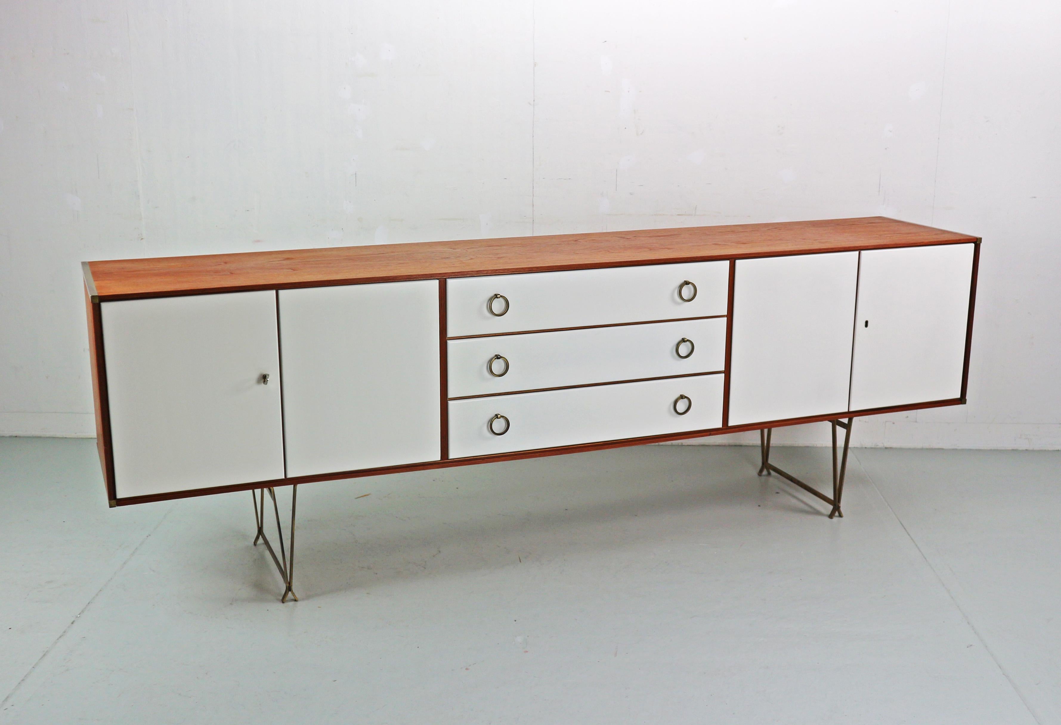 Mid- Century modern period side-board or other words buffet cabinet designed by William Watting and manufactured for Fristho in 1950's period, The Netherlands.

Cabinet is made of teak wood with four white lacquered doors and beautiful brass details