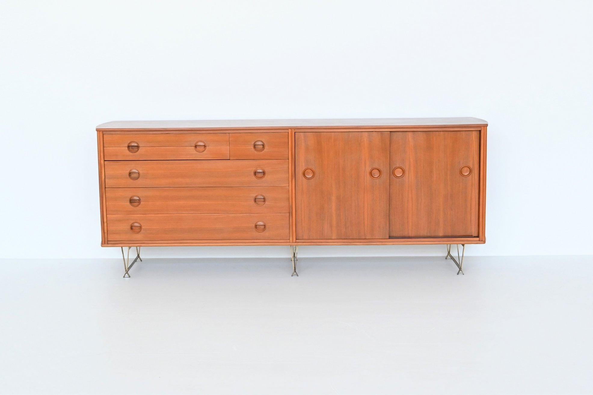 Stunning and rare sideboard designed by William Watting and manufactured by Fristho, The Netherlands 1954. This very nice shaped sideboard is made of veneered walnut wood with brass legs. On the right it has two sliding doors with shelves behind and