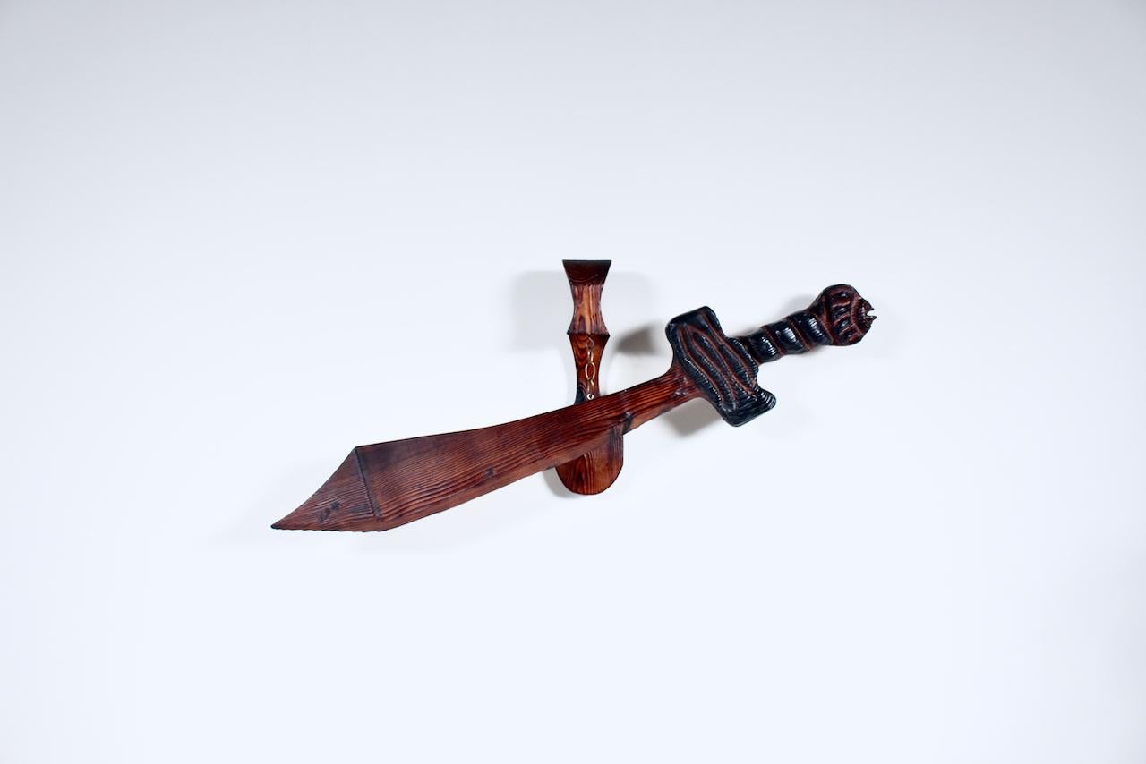 William Westenhaver WITCO hand carved Wall Mount Wooden Sword. Featuring a large, handcrafted tropical style grained, stained solid wood Sword with Black enamel to handle, attaching to matching wood wall mount measuring: 19H x 8W x 6D, and suspended