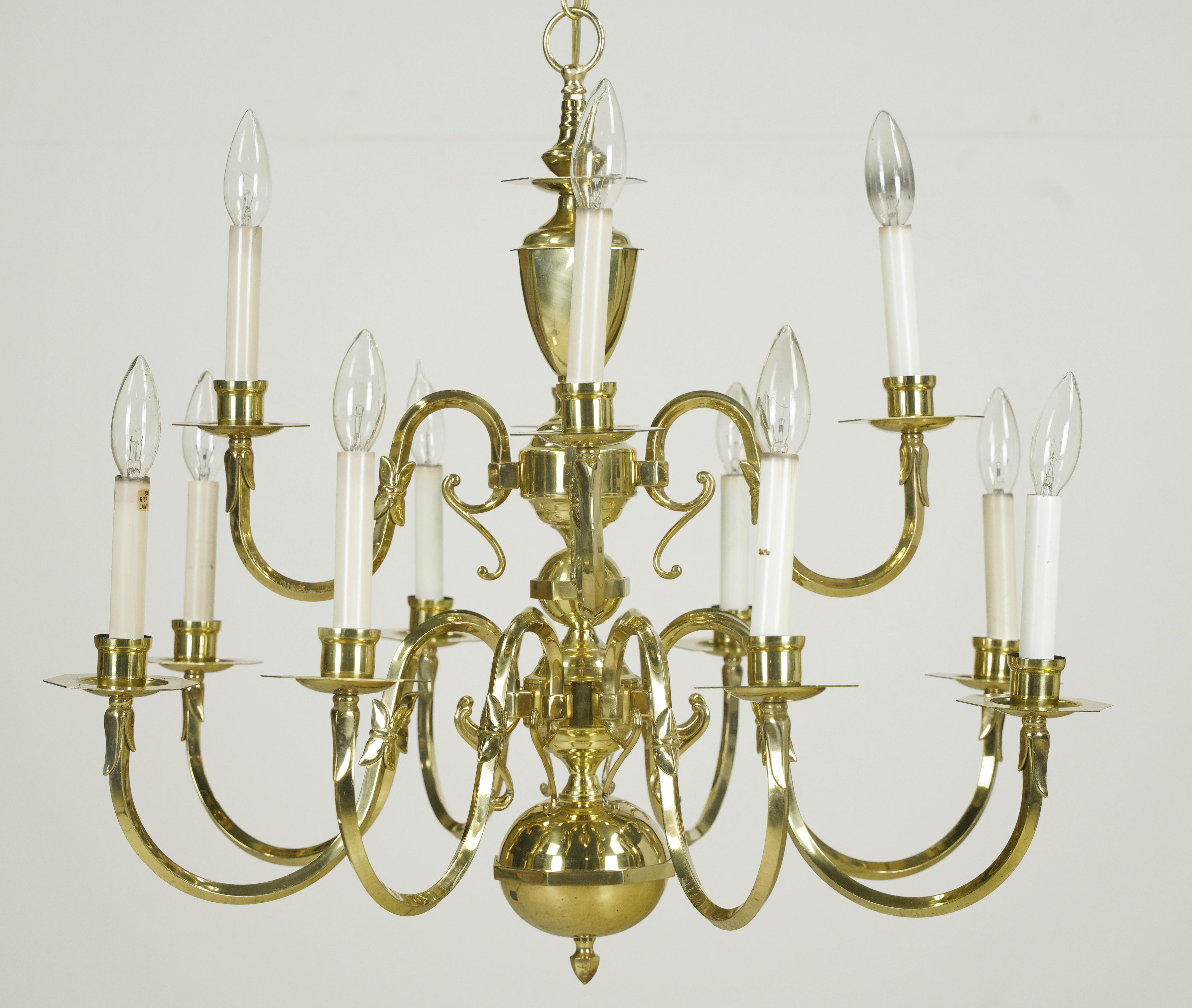 Lampadario a due piani Williamsburg in ottone lucido con dodici bracci. In buone condizioni, presenta un'usura superficiale dovuta all'uso precedente, con una certa deformazione dei bracci e una leggera ammaccatura sul tettuccio. Questa lampada