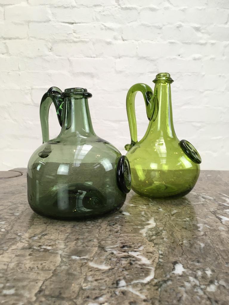 A pair or Jamestown reproduction flasks with handles. These date from the 1960s. They are mouth-blown reproductions using traditional 17th century methods. They follow the style of the Williamsburg VA bottles - an archaeological discovery of early