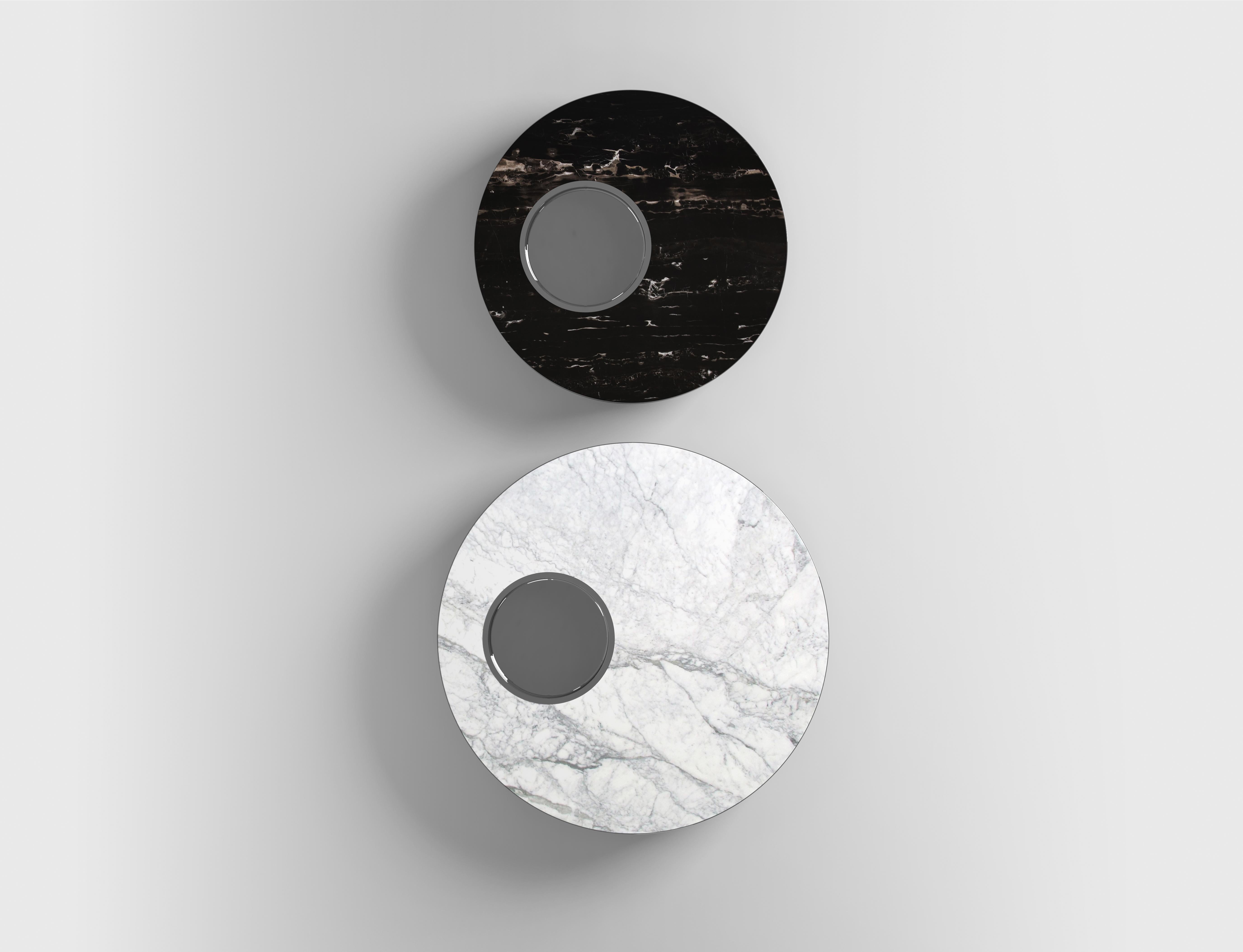Il s'agit d'une table basse ronde moderne au design minimaliste et élégant. Le plateau de la table semble être en marbre avec une surface gris clair présentant des motifs de veines naturelles, ce qui ajoute une touche sophistiquée. La table présente
