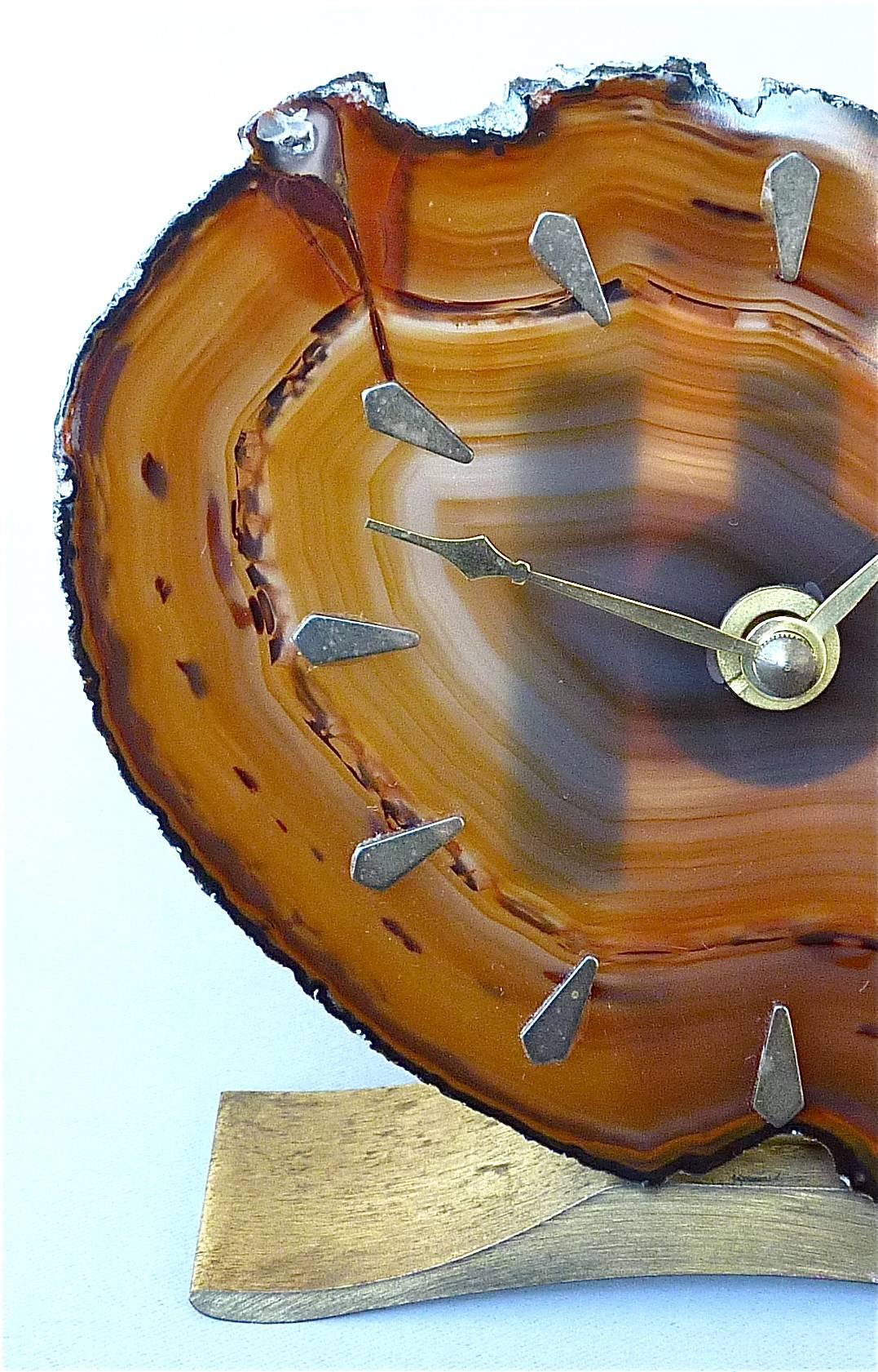 Magnifique horloge de table sophistiquée à attribution Willy Daros, Belgique et Allemagne, vers les années 1970. Elle possède une belle face en agate (pierre polie) de couleur ambre à miel avec des repères de 12 heures en laiton, montée sur une base