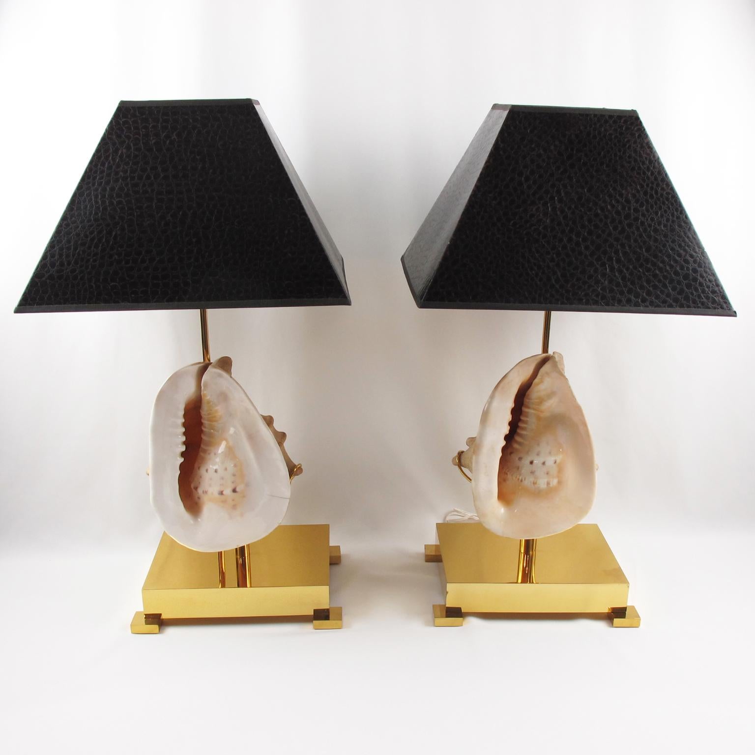 Willy Daro designed these stunning table lamps in the 1970s. This pair of lamps boast oversized sea shells mounted on a square polished brass base. 
The lampshades are geometrically shaped in dark brown color with a textured faux crocodile skin