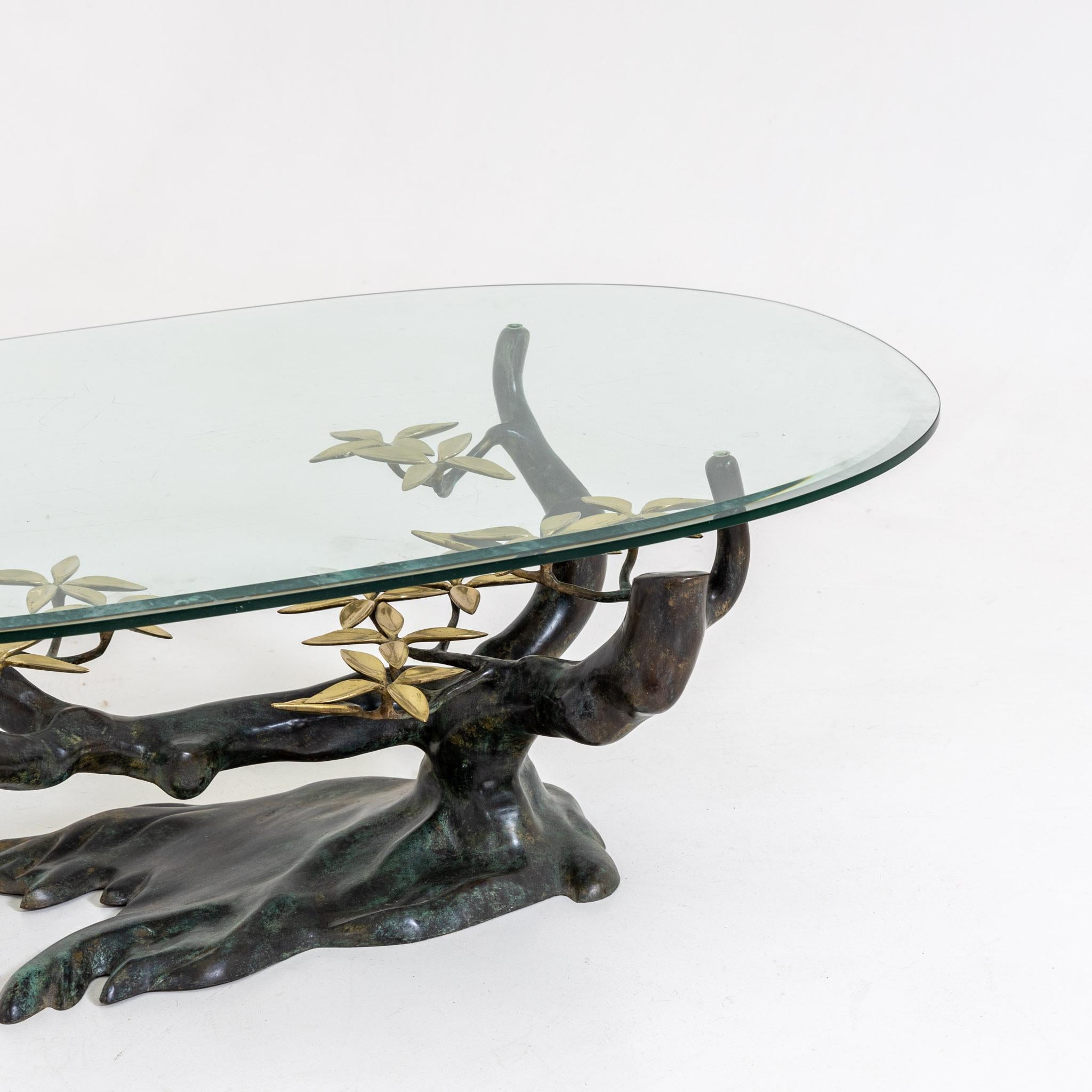 Coffee table by Willy Daro with bronze base in the form of a stylized bonsai with gold-colored leaves and oval glass top with slight facet cut on the edge.
