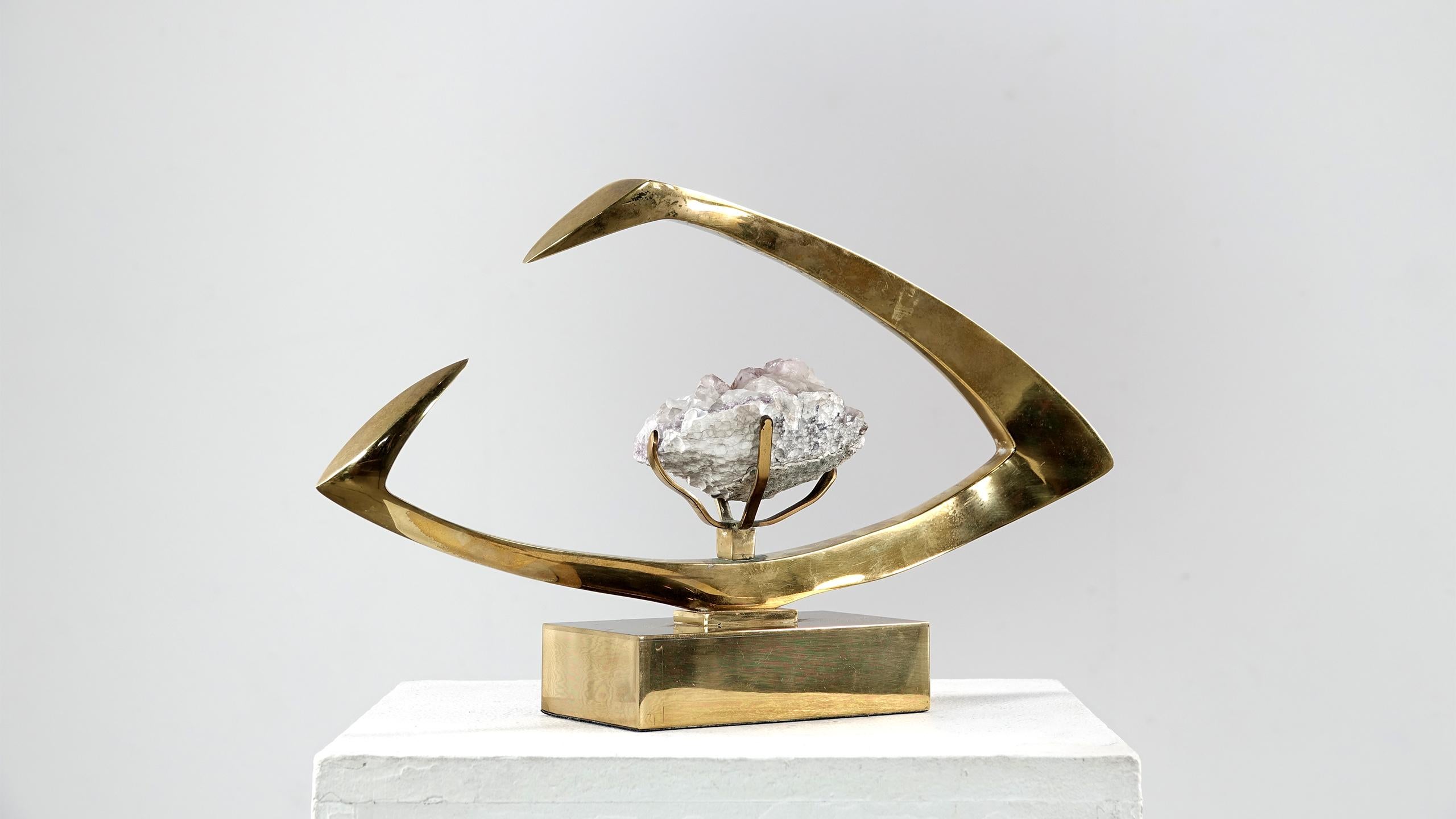 This amazing signed sculpture was created by Willy Daro in the 1970s. On a rectangular plinth with a transversal oval setting, inside it is a large crystal.
The Belgian artist Willy Daro loved to work with brass in combination with mineral