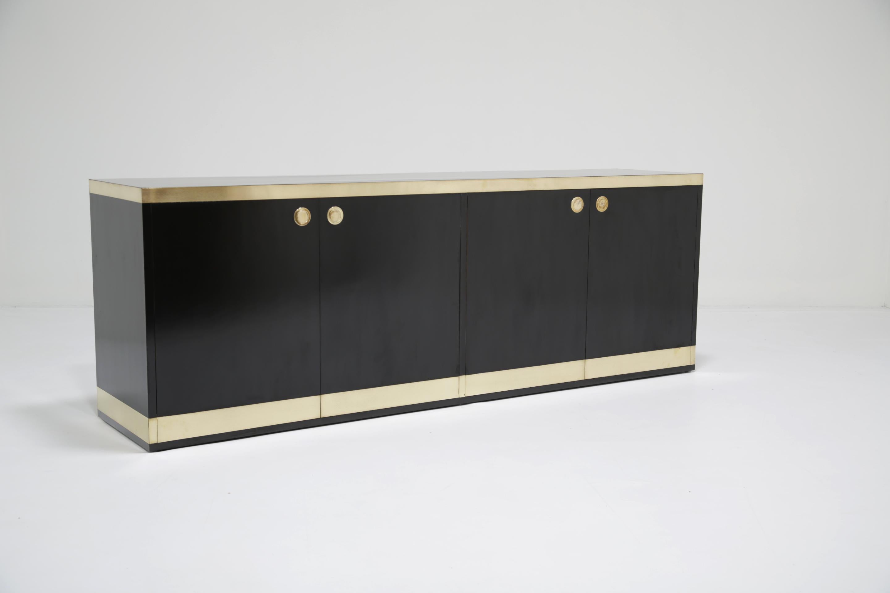 Disegnata da Willy Rizzo negli anni '70, questa elegante e scultorea credenza in formica nera è accentuata da un'audace fascia in ottone spazzolato lungo il piano e la base, creando un ricco contrasto che risulta allo stesso tempo glamour e