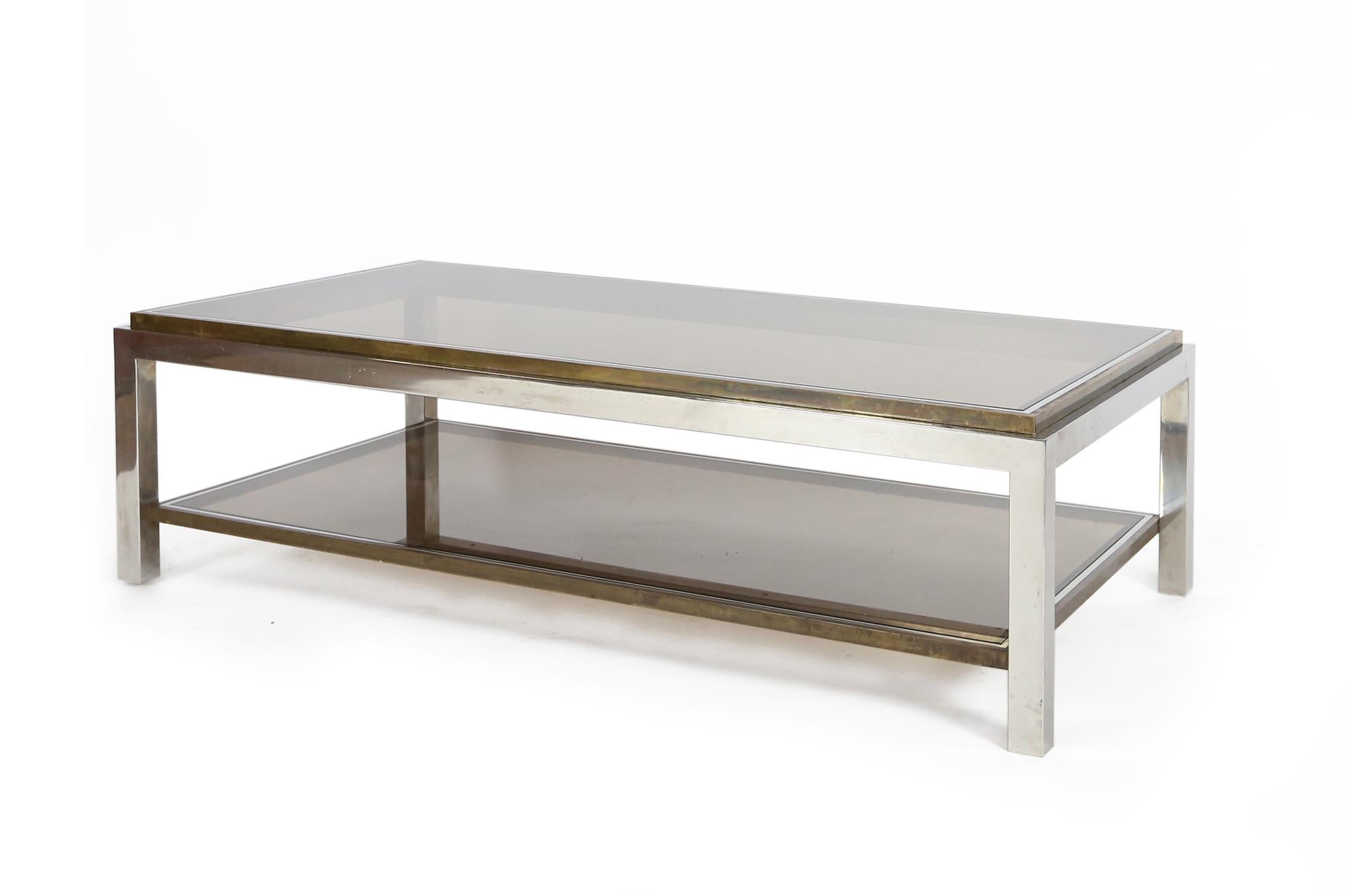 Rectangular two-tiered coffee table with stepped brass trim holding the smoked glass, raised on a chrome frame.
 