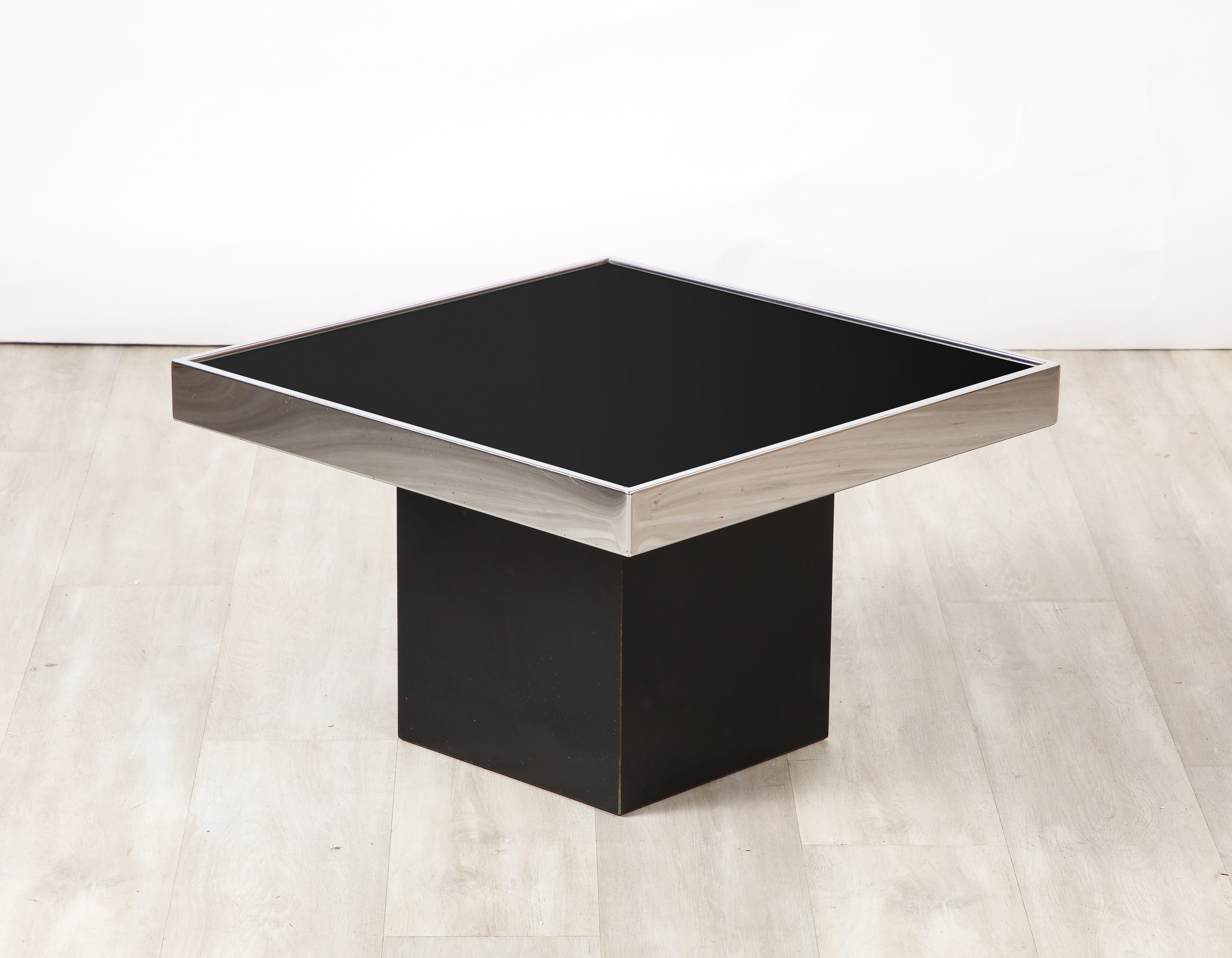 A Willy Rizzo for Cidue square side/end/or coffee table; with a sleek and seamless design.  The chic black glass surface is inset to the chrome square apron and supported on a black plinth base.  Very glamourous and timeless design, highly