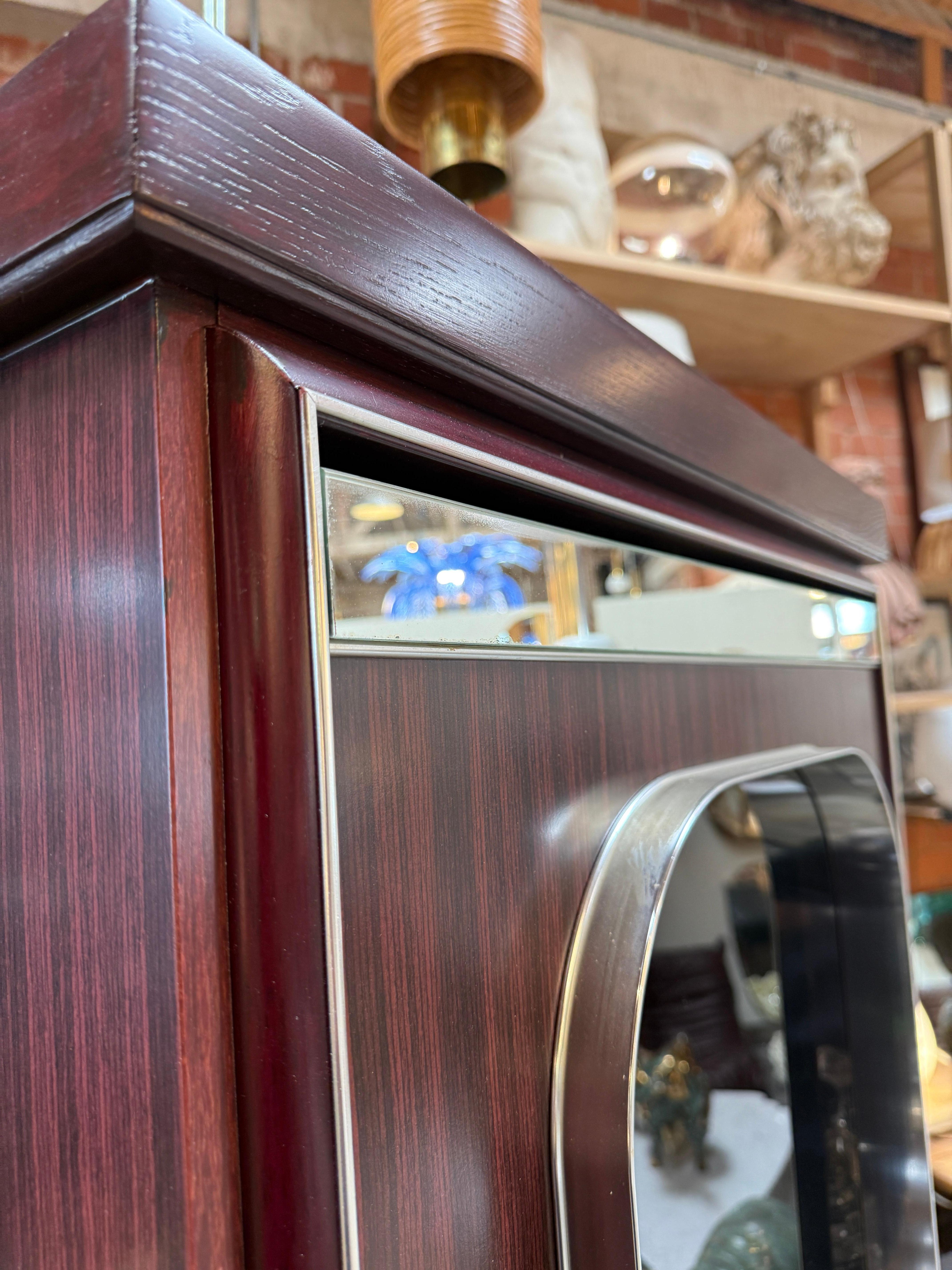 A rare illuminated display cabinet designed attributed to Willy Rizzo in the 1970s. The piece is crafted in rich rosewood veneer with chrome detailing and features three beveled glass windows with mirrored back panels. Internal lighting highlights