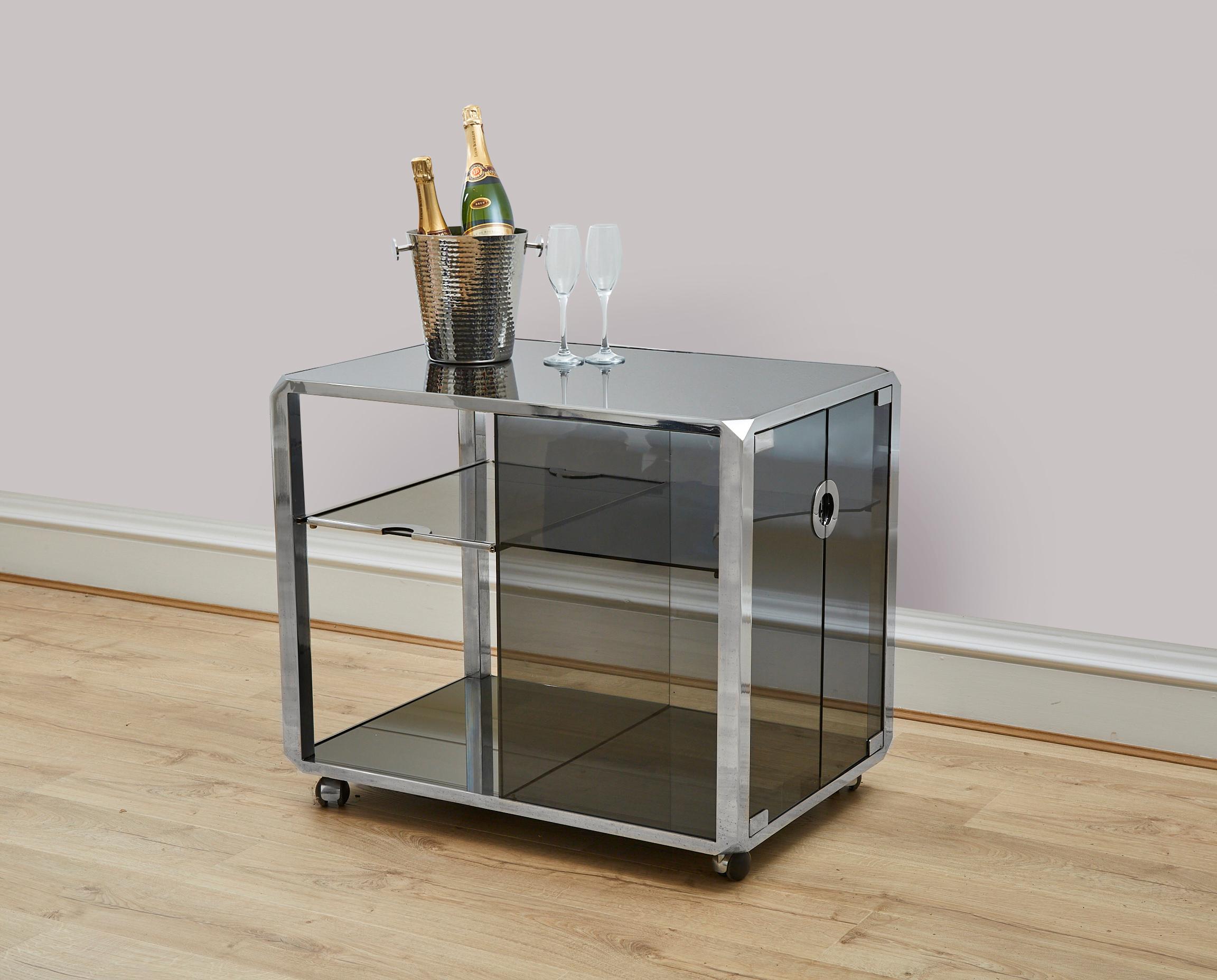 A super stylish mid century modern drinks cart / drinks bar featuring polished chrome and smoked glass.
This bar was produced in the 1970's and designed by Renowned Italian furniture designer Willy Rizzo who is celebrated for having produced