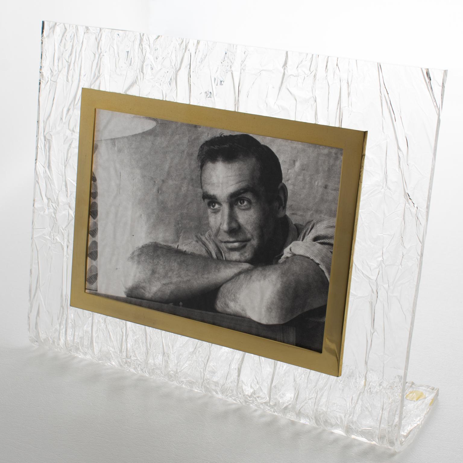 Ce magnifique cadre photo moderniste en Lucite et laiton présente un design attribué aux œuvres de Willy Rizzo. Fabriquée en Italie vers 1970, cette ravissante pièce décorative présente une forme en 