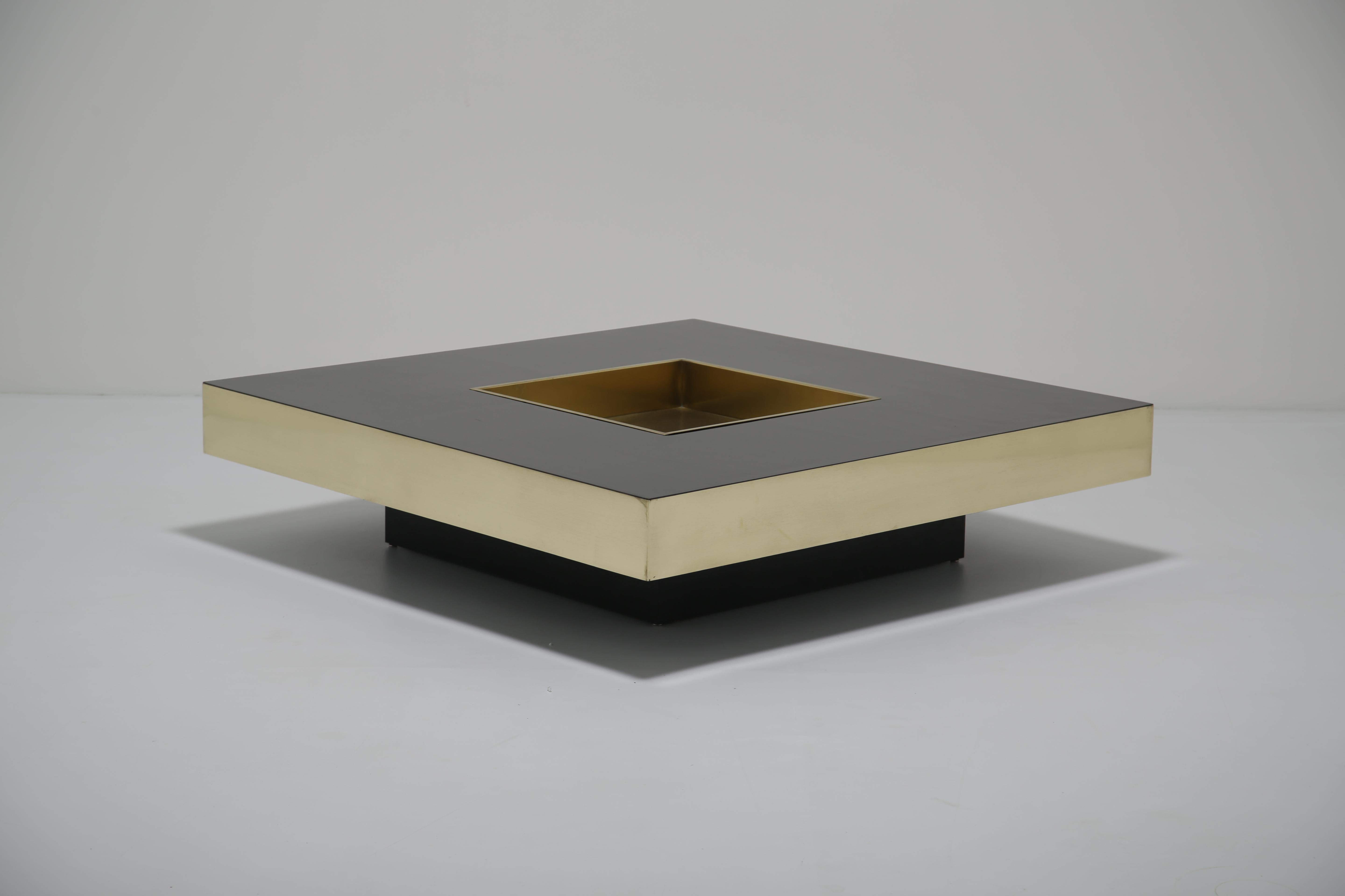 A striking Italian coffee table from the 1970s, attributed to Willy Rizzo. The square form is finished in black Formica and accented with brass trim, creating a bold contrast that epitomises the era’s glamorous modernist aesthetic. At its centre, a
