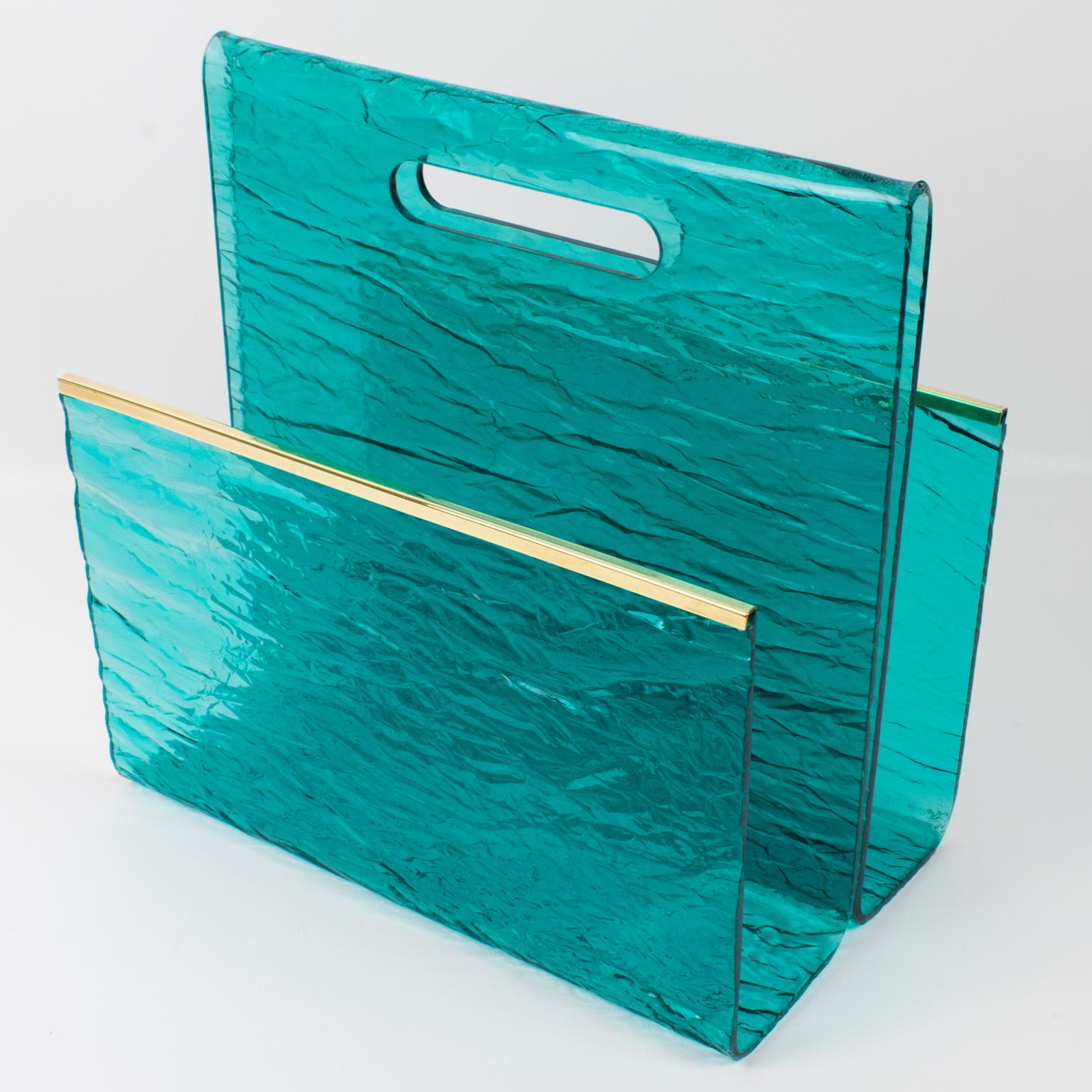 This handsome 1970s modernist magazine rack or holder has its design attributed to Willy Rizzo. The geometric shape boasts a gilded brass metal gallery and turquoise blue-lagoon textured pattern Lucite. The crystal transparent Lucite has a stunning