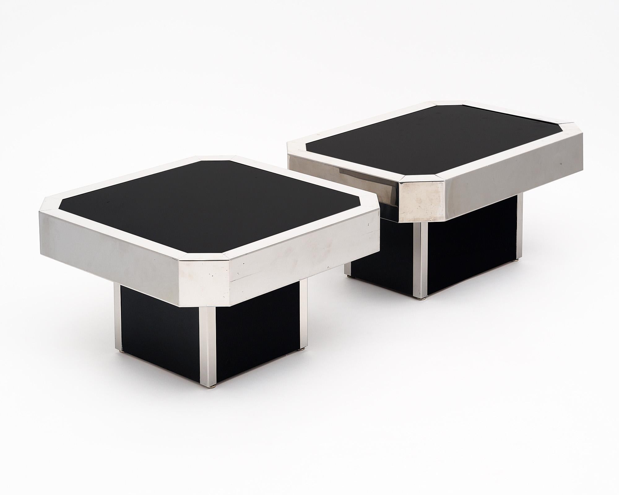 Pair of side tables in the style of renowned designer and artist Willy Rizzo. This pair is from Italy and features the iconic shape, a rectangle or square with cut corners. Each has a black glass top completely trimmed with chrome. One is a longer