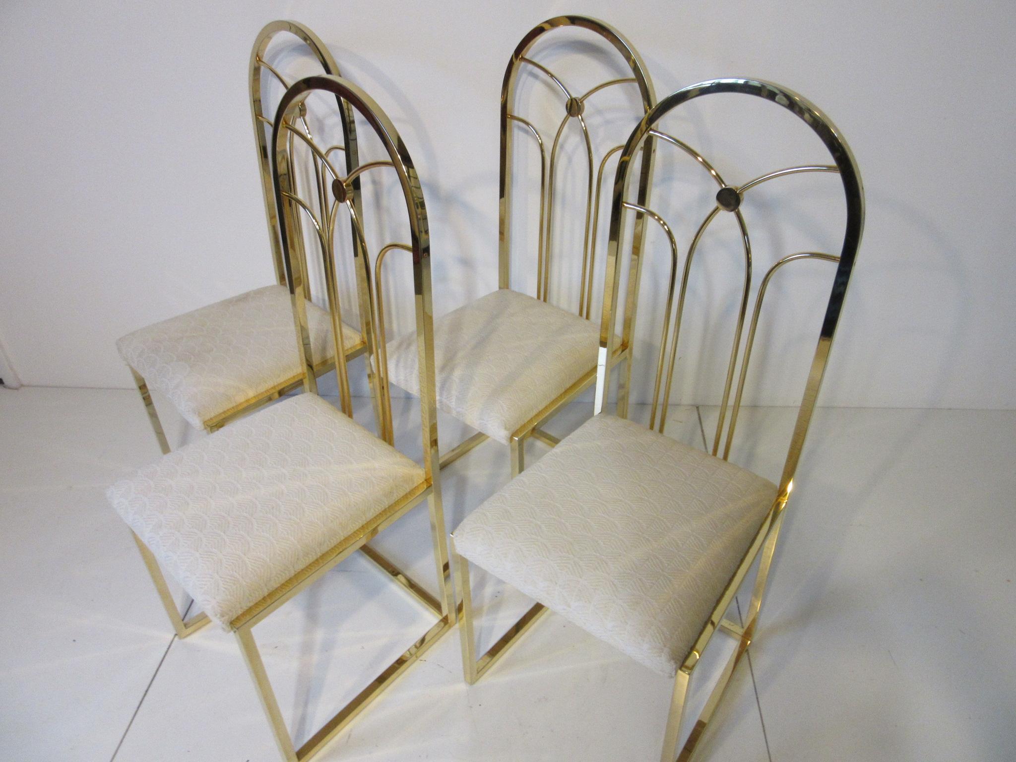 A set of four gold gilded dining chairs with square metal frames, decor back rests and upholstered seat cushions in the manner of Willy Rizzo .