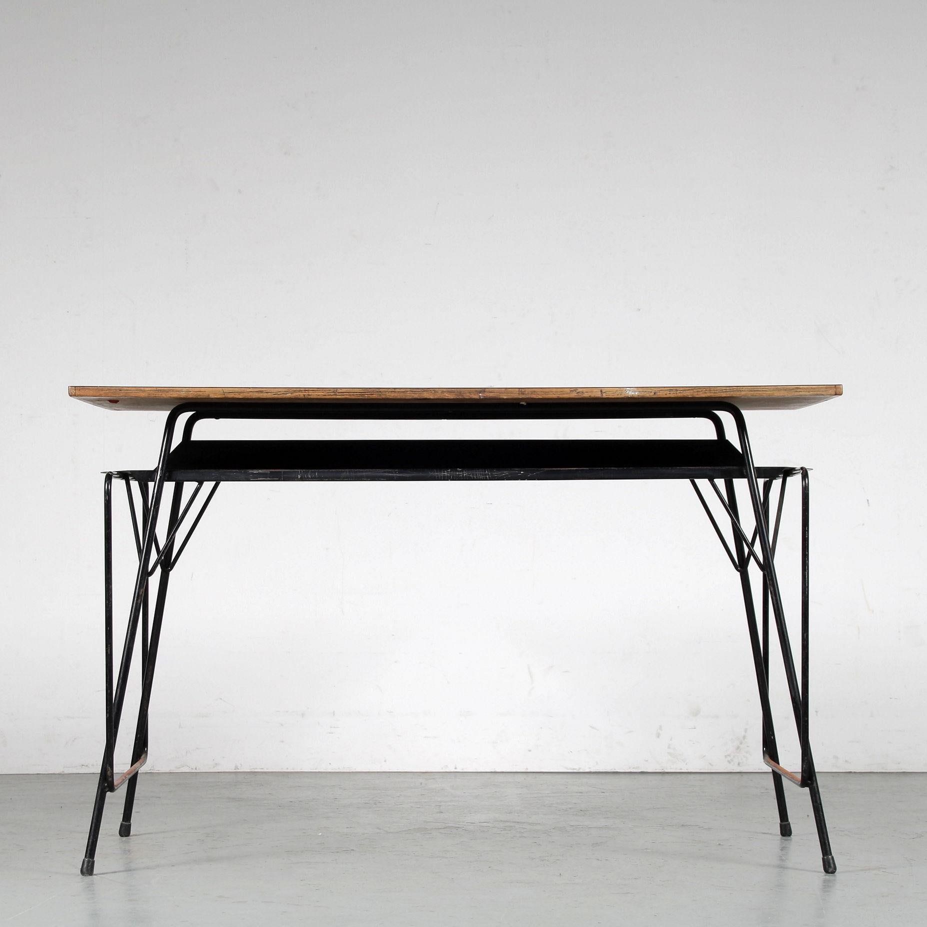 A beautiful teacher’s desk designed by Willy van der Meeren, manufactured by Tubax in Belgium around 1950.

The table has a thin black lacquered metal base with a grey formica top. Underneath the top, there’s the black metal shelf that functions