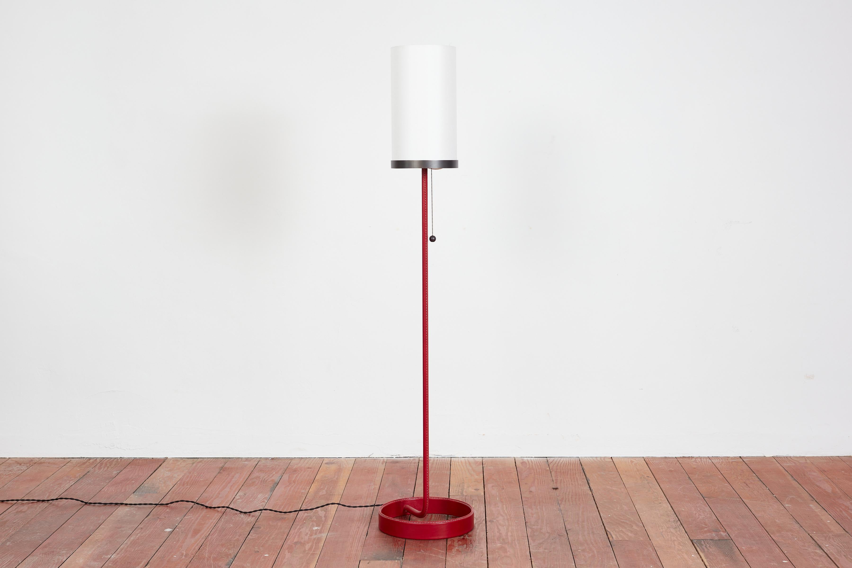Classic floor lamp with circular base and pole covered in red leather with white contrast stitching. Iron ball on pull chain and silk shade. 

Available in black, chocolate, and cognac leather. 

Shade available in white or ivory silk. 

Made in Los