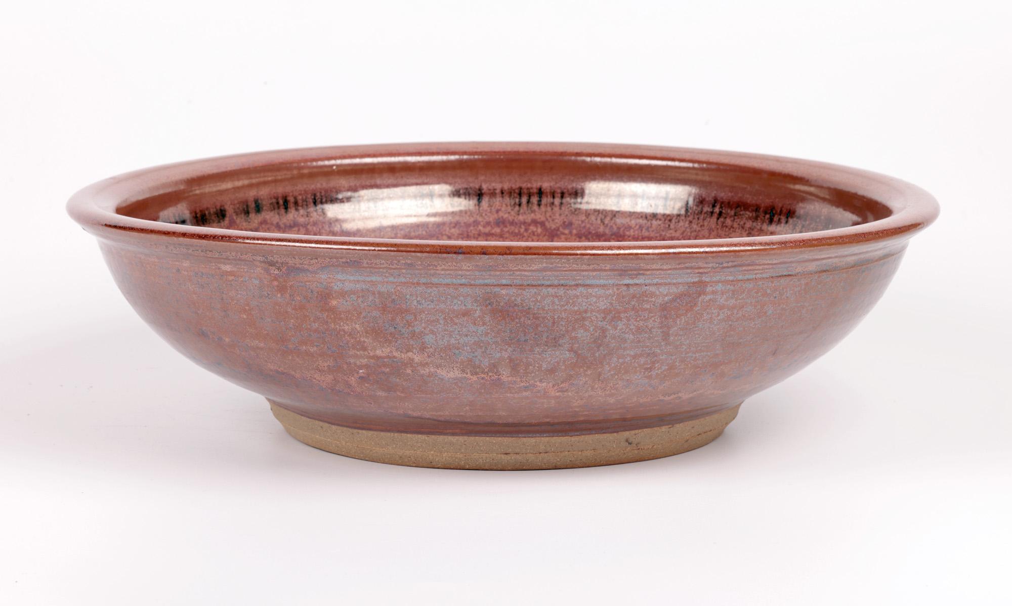 A large and impressive Winchcombe studio pottery bowl with slip trailed patterning and copper glazes attributed to Ray Finch and dating from the latter 20th century. The hand thrown bowl is heavily made and stands raised on a narrow unglazed round