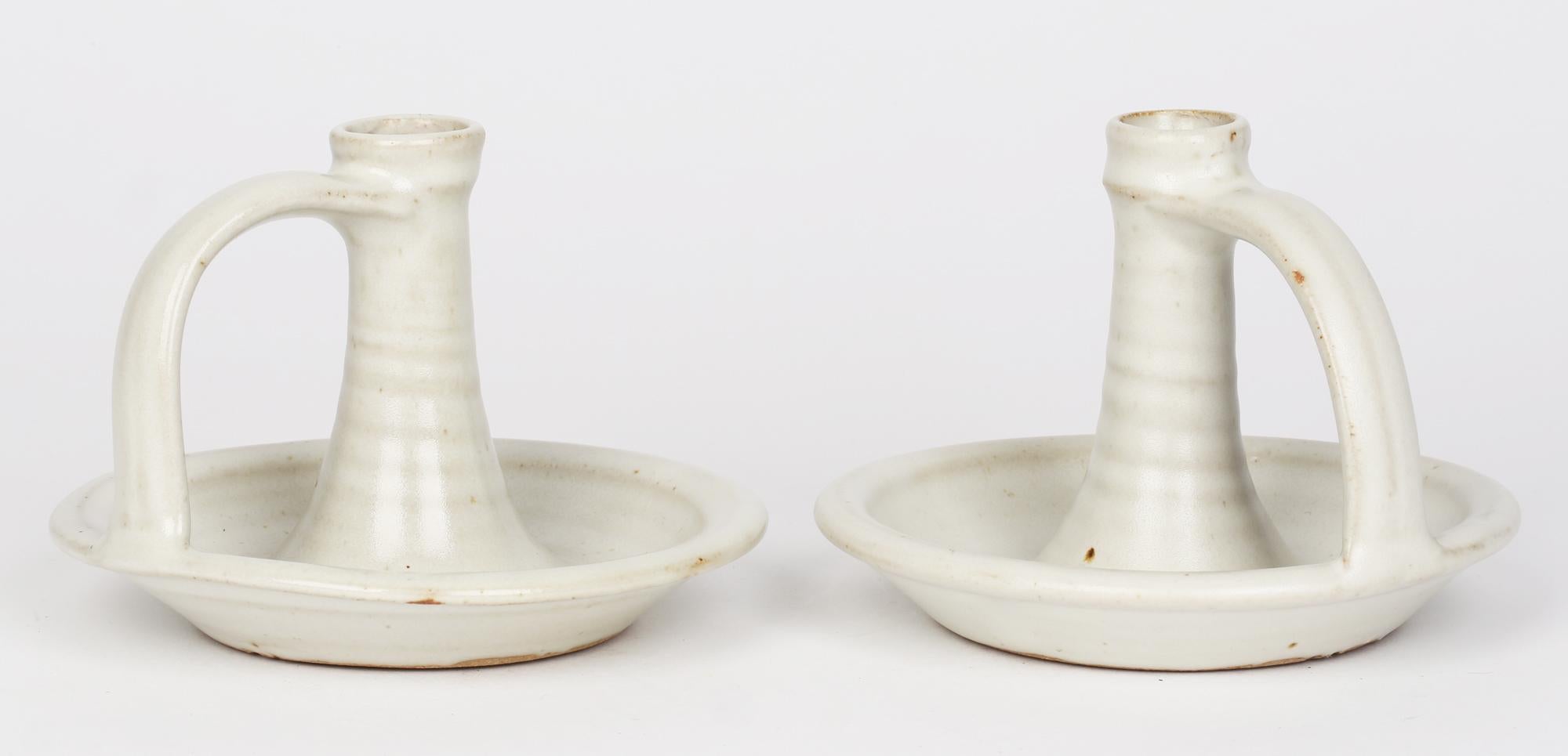 A pair Winchcombe Pottery wood fired studio pottery chamber sticks decorated in oatmeal glazes dating from the 20th century. The chambersticks have a wide bowl shaped base with a raised rim and with a raised hollow candle holder to the center with a
