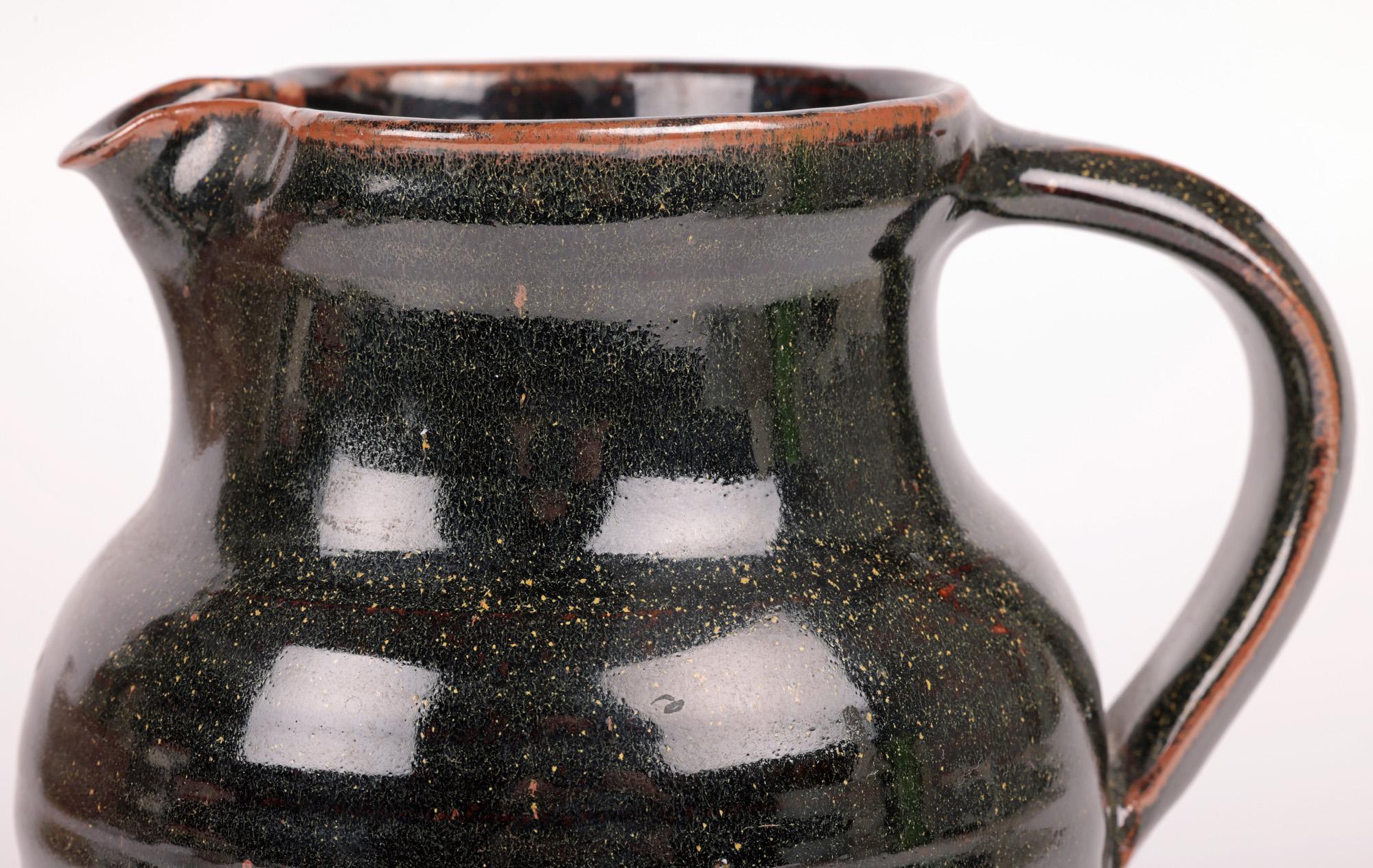 A fine tenmoku glazed studio pottery jug probably by Ray Finch and made at the acclaimed Winchcombe Pottery in Gloucestershire, England in the latter 20th century. The hand thrown jug is of round bulbous shape standing on a flat narrow round