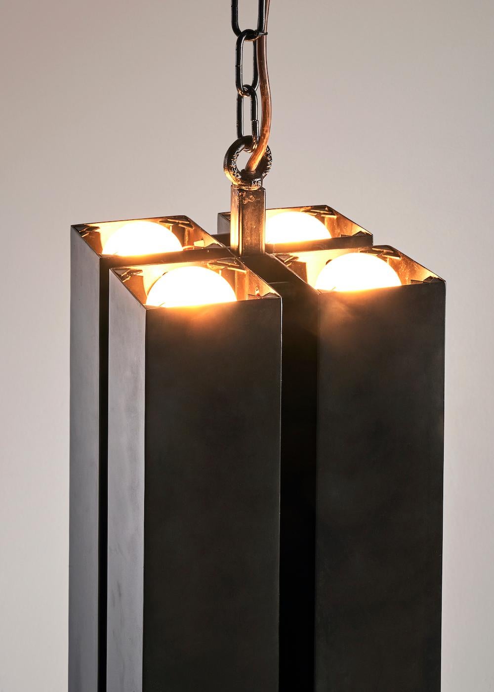 This is a custom pendant with a blackened brass body. LED light bulbs within the fixture create an uplight and a downlight effect. Choices of material are patina'ed brass or stainless steel bodies. Each fixture is designed and made to each client's
